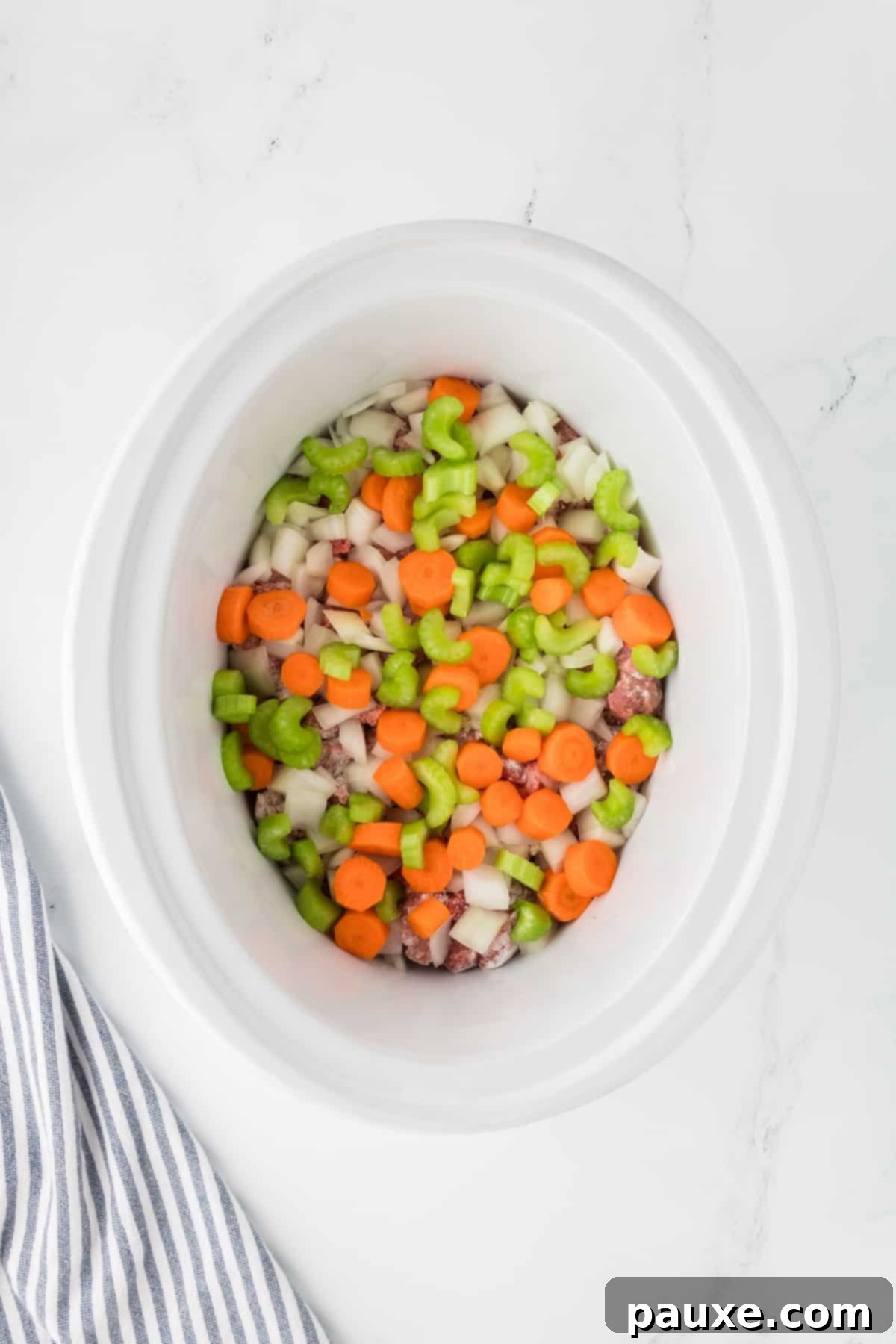 Comforting Slow Cooker Beef Stew and Dumplings 5 A slow cooker with layers of floured beef cubes, chopped celery, sliced carrots, and diced onions inside.