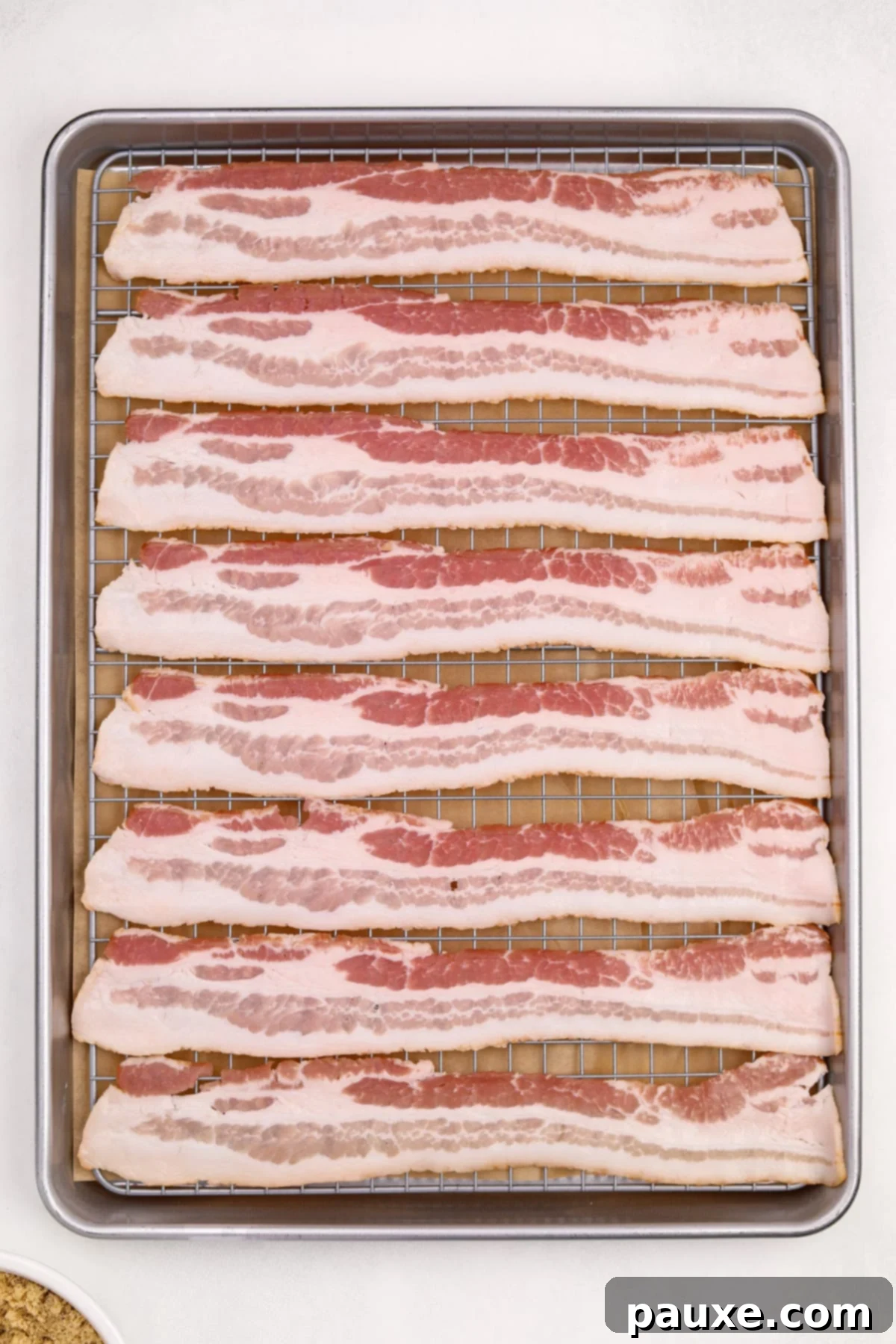 Crispy Caramelized Bacon 6 Raw bacon strips in an even layer on a wire rack set inside of a baking pan.