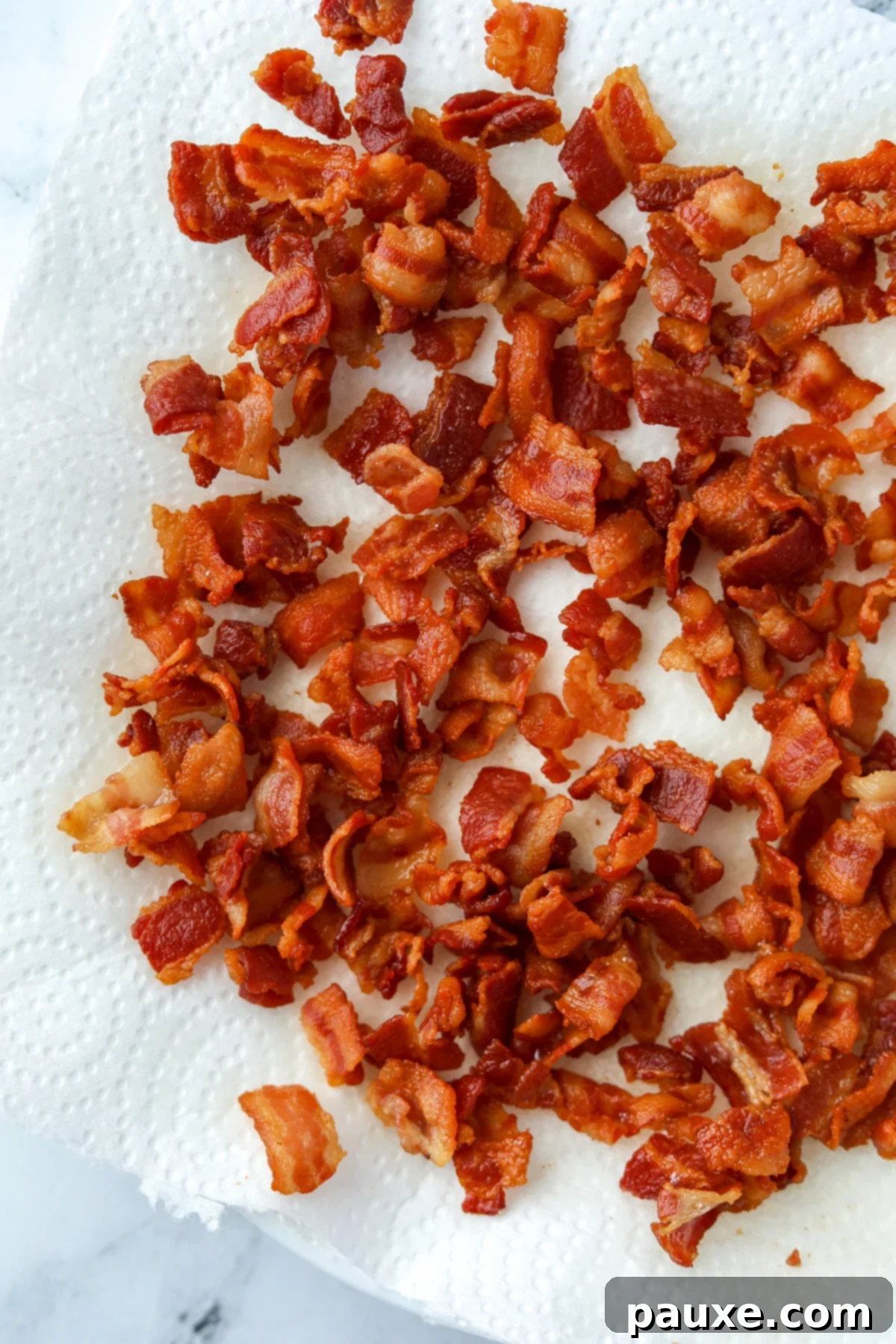 Crafting Crispy Homemade Bacon Bits 8 A mound of freshly cooked homemade bacon bits, golden and crispy, carefully draining excess grease on a generous layer of paper towels.