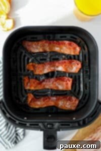 Crispy Air Fryer Bacon 12 Cooked bacon slices in an air fryer basket on a white counter.