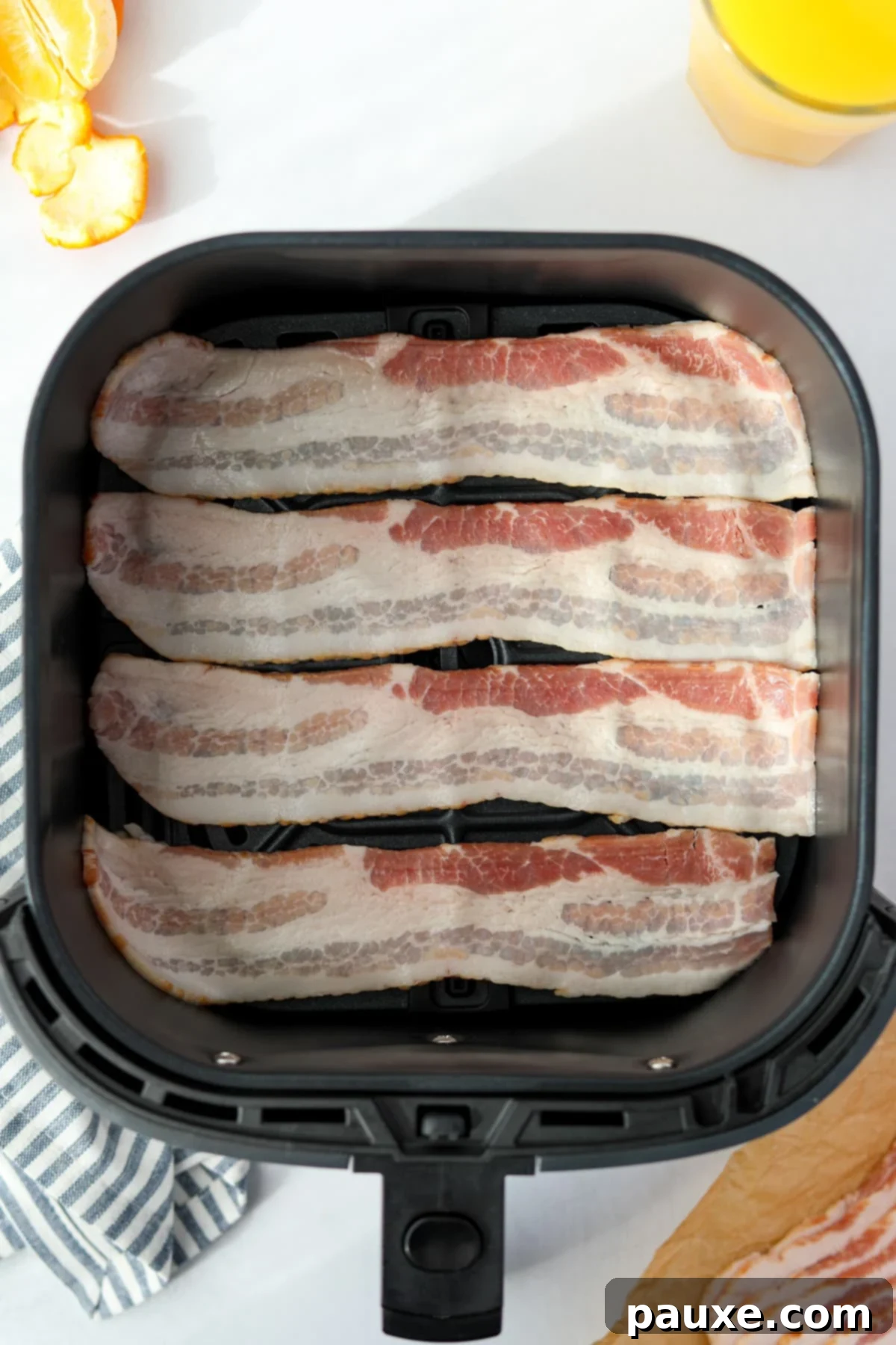Crispy Air Fryer Bacon 4 Raw bacon slices carefully placed in a single layer inside an air fryer basket.