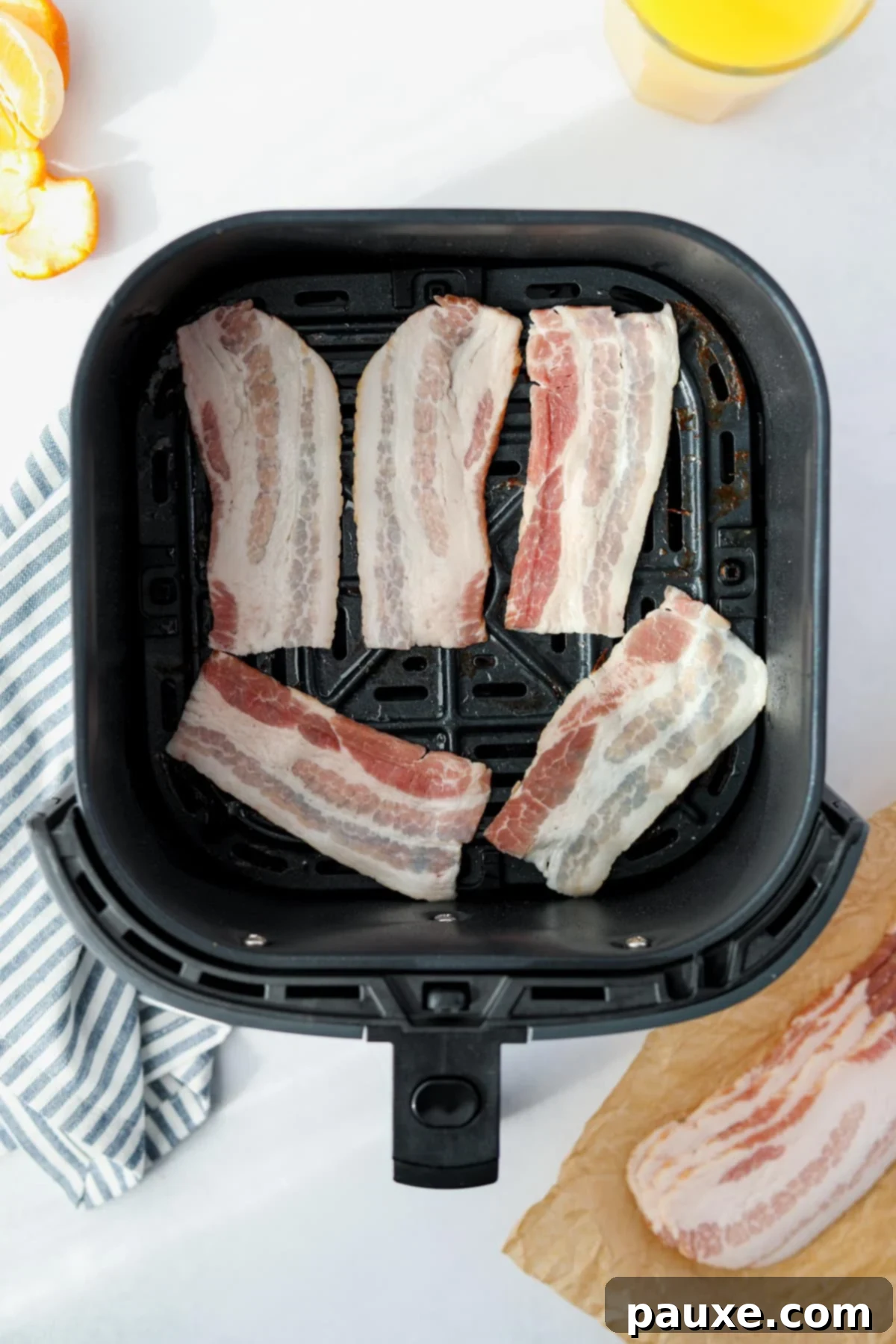 Crispy Air Fryer Bacon 6 Half slices of raw bacon laid out in a single layer in an air fryer basket.