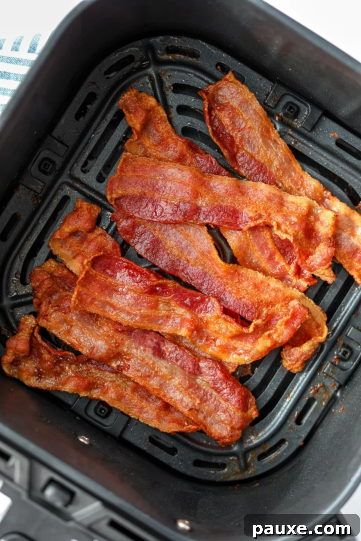Crispy Air Fryer Bacon 9 Three strips of crispy air fryer bacon resting on a white plate, ready for a delicious breakfast.