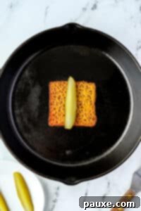 Zesty Brined Cheese Bites 13 Placing a dill pickle spear in the middle of a slice of melted and crispy cheese in a pan.