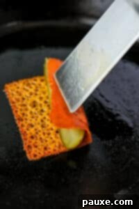 Zesty Brined Cheese Bites 14 Rolling crispy cheese over a pickle spear using a spatula, showing the wrapping process.