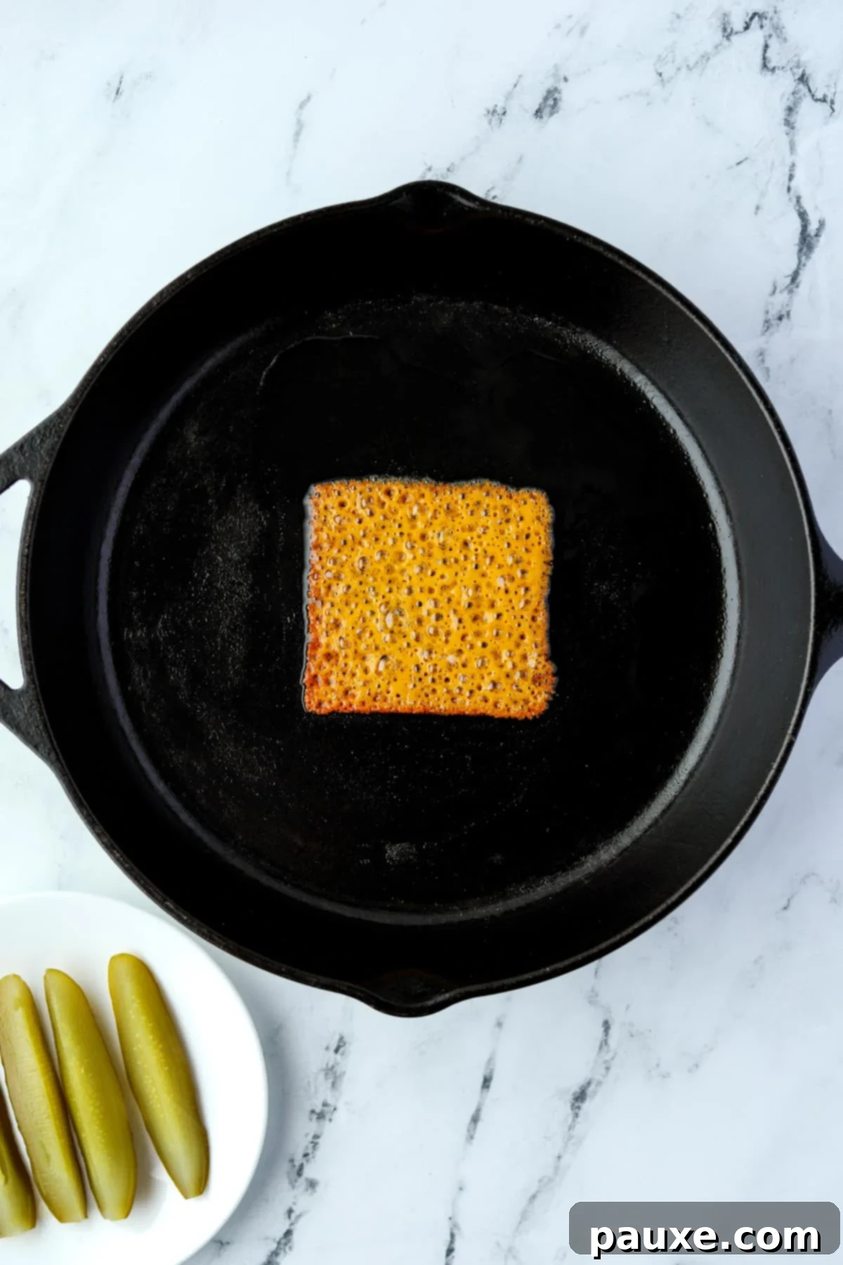 Zesty Brined Cheese Bites 4 A non-stick skillet with a single slice of cheese melting in the center, beginning to crisp and brown around the edges.