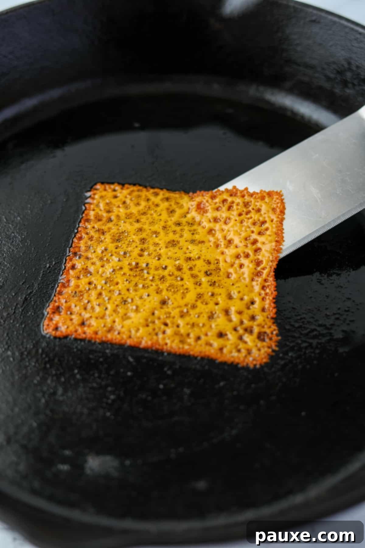 Zesty Brined Cheese Bites 5 A thin spatula gently loosening the edges of a melted and browning cheese slice from the pan, ensuring it doesn't stick.
