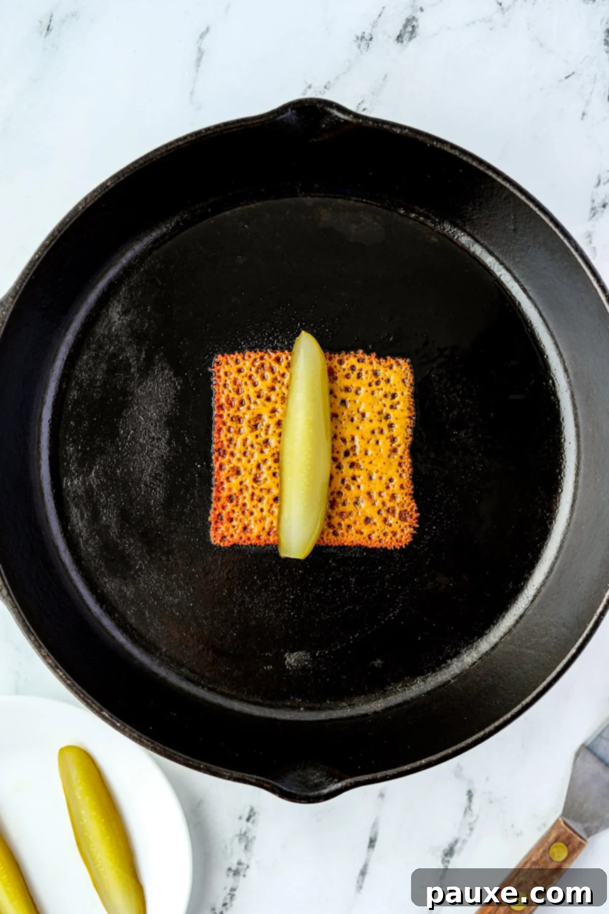 Zesty Brined Cheese Bites 6 A dill pickle spear being carefully placed onto the center of a melted and crispy cheese slice in a hot skillet.