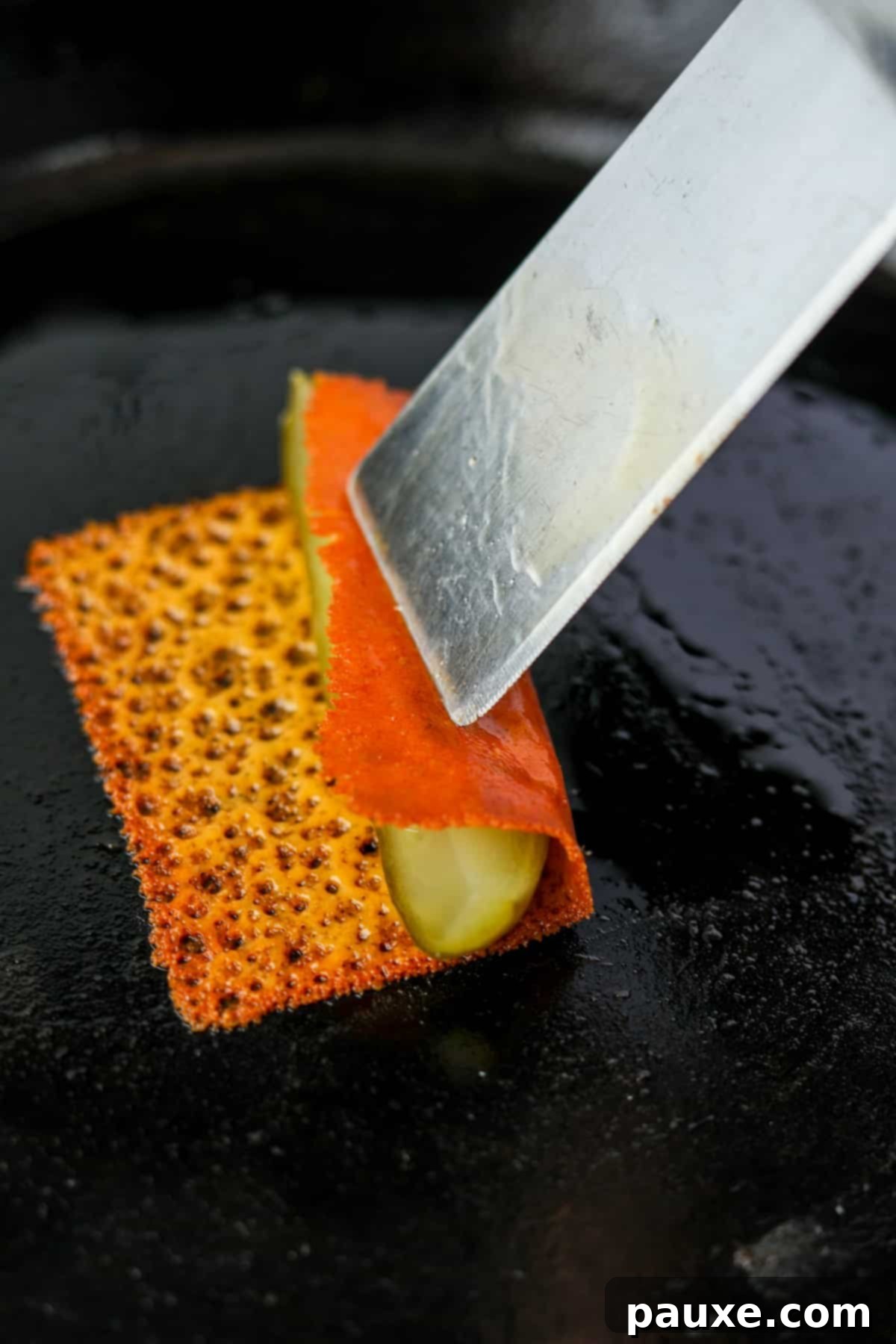 Zesty Brined Cheese Bites 7 A spatula rolling one side of the crispy cheese over a pickle spear, beginning to wrap it completely.