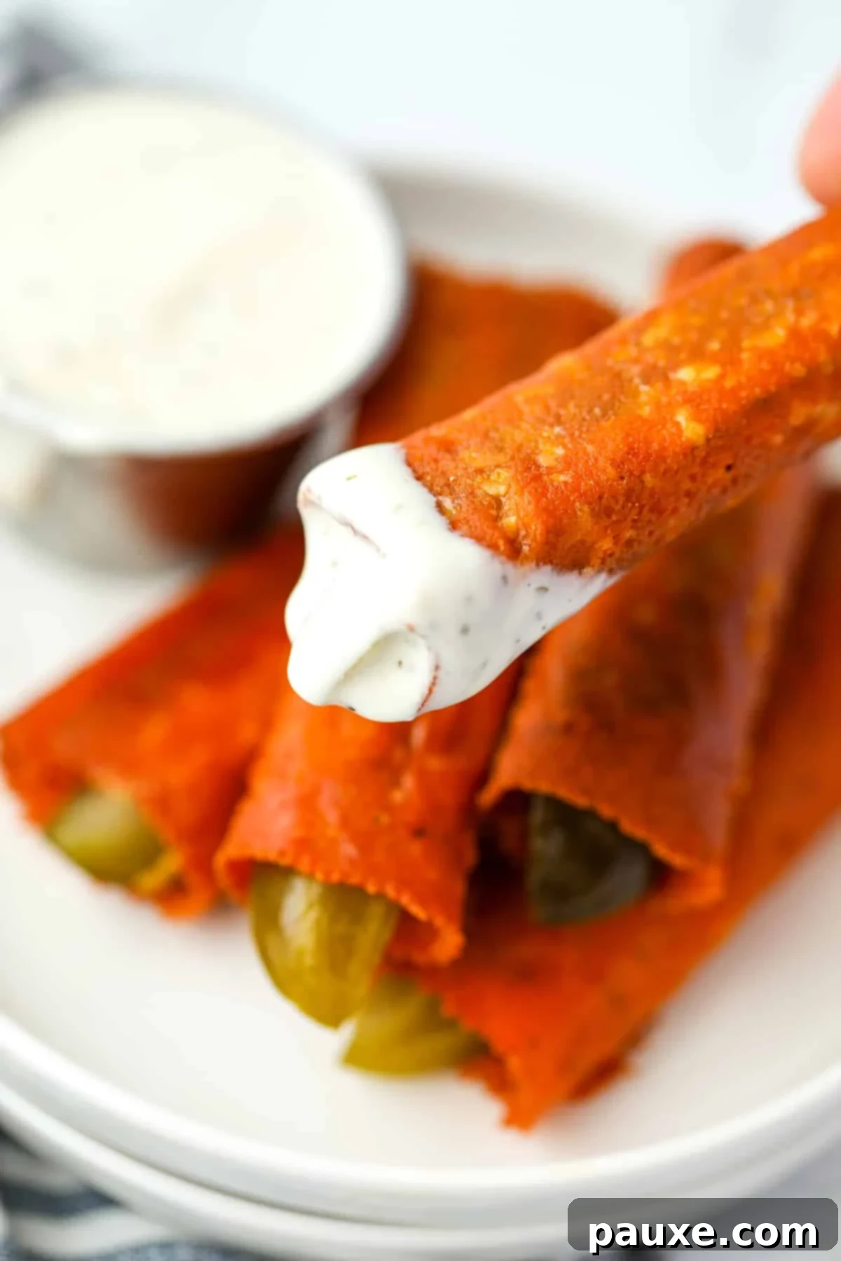 Zesty Brined Cheese Bites 8 A hand dipping a golden-brown crispy cheese pickle into a small bowl of creamy ranch dressing, highlighting its appealing texture.