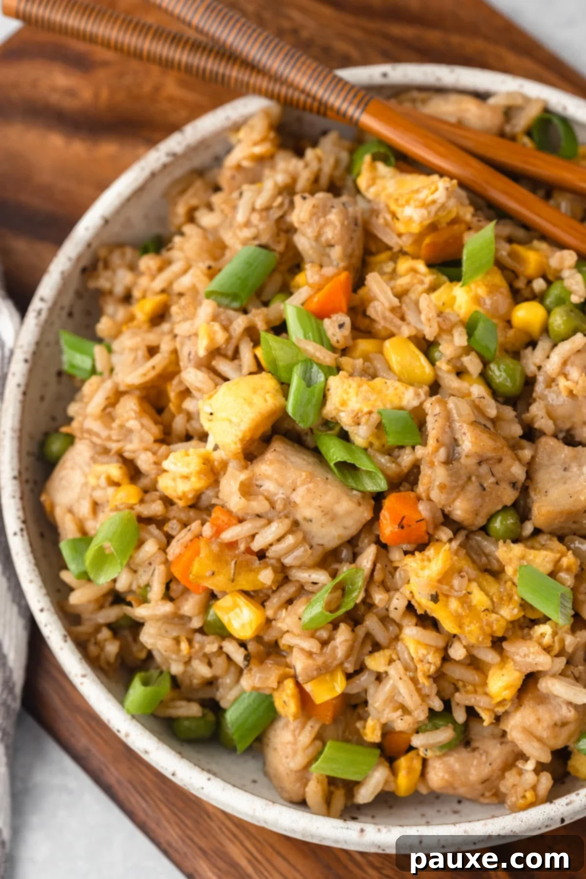 The Art of Benihana Chicken Fried Rice 5 A close-up shot of a bowl of chicken fried rice, garnished with green onions, with chopsticks ready to pick up a serving.