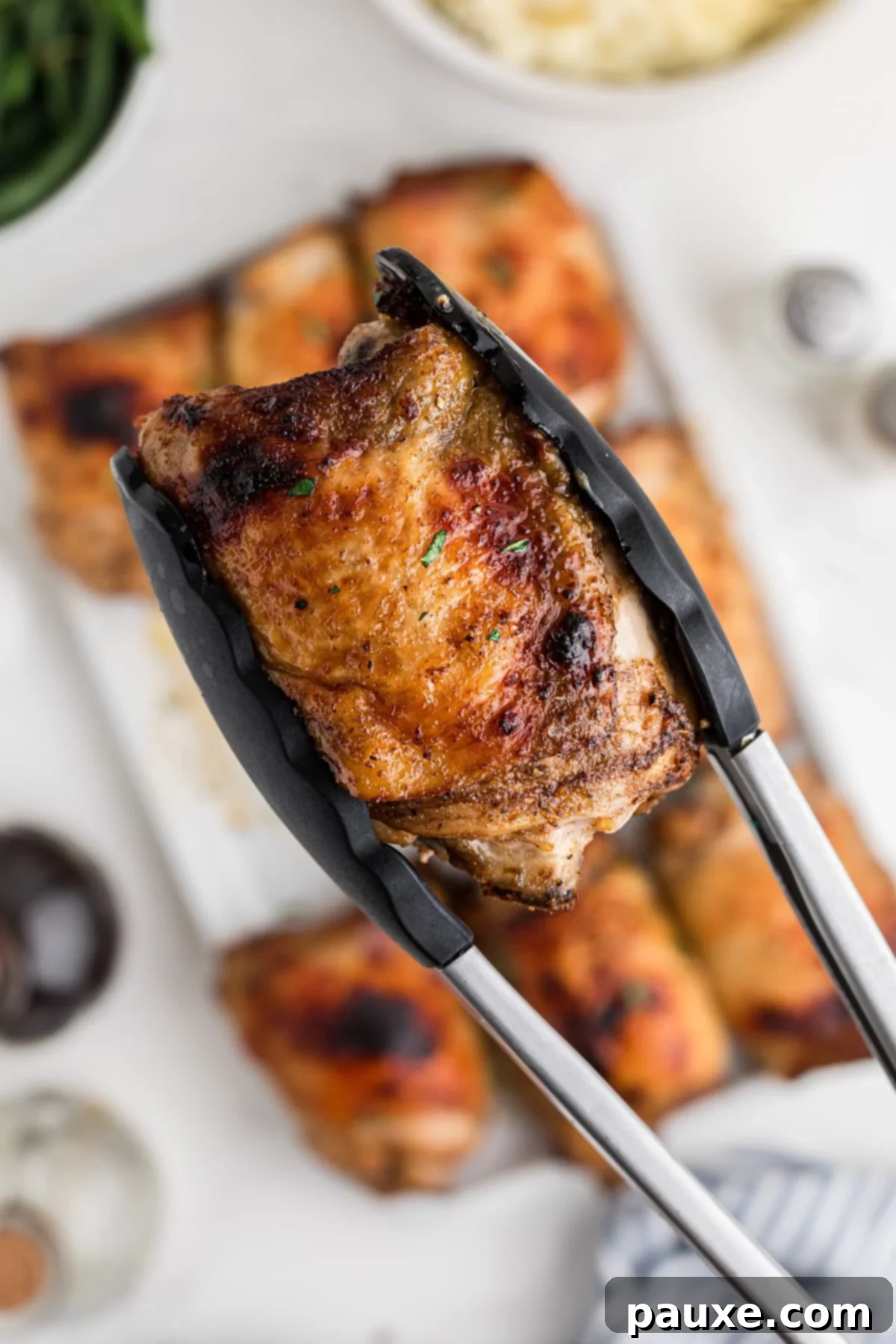 Mastering Chicken Marinades 9 A pair of tongs lifting up a baked chicken thigh.