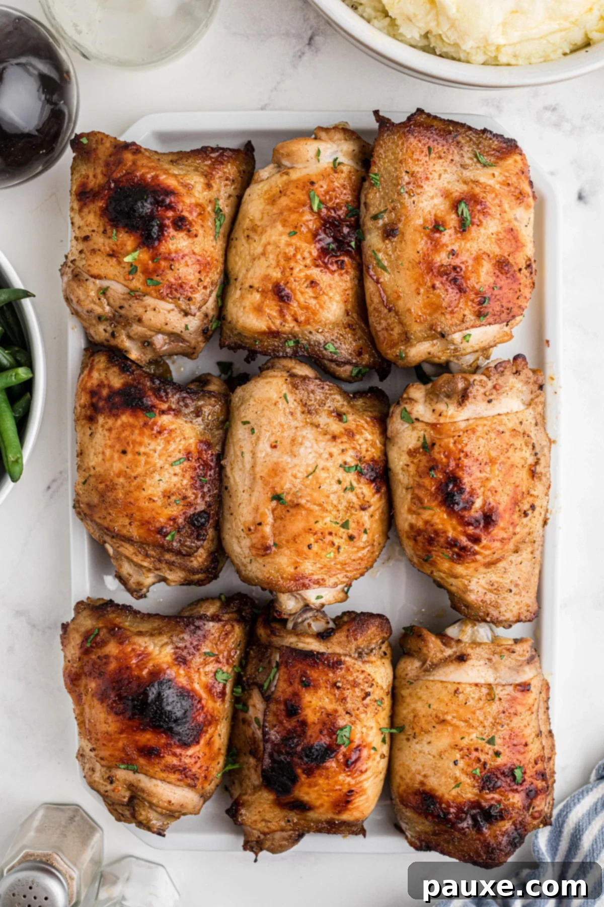 Golden Baked Chicken Thighs 2 A serving platter filled with 9 chicken thighs that have been baked until crispy, garnished with fresh herbs.