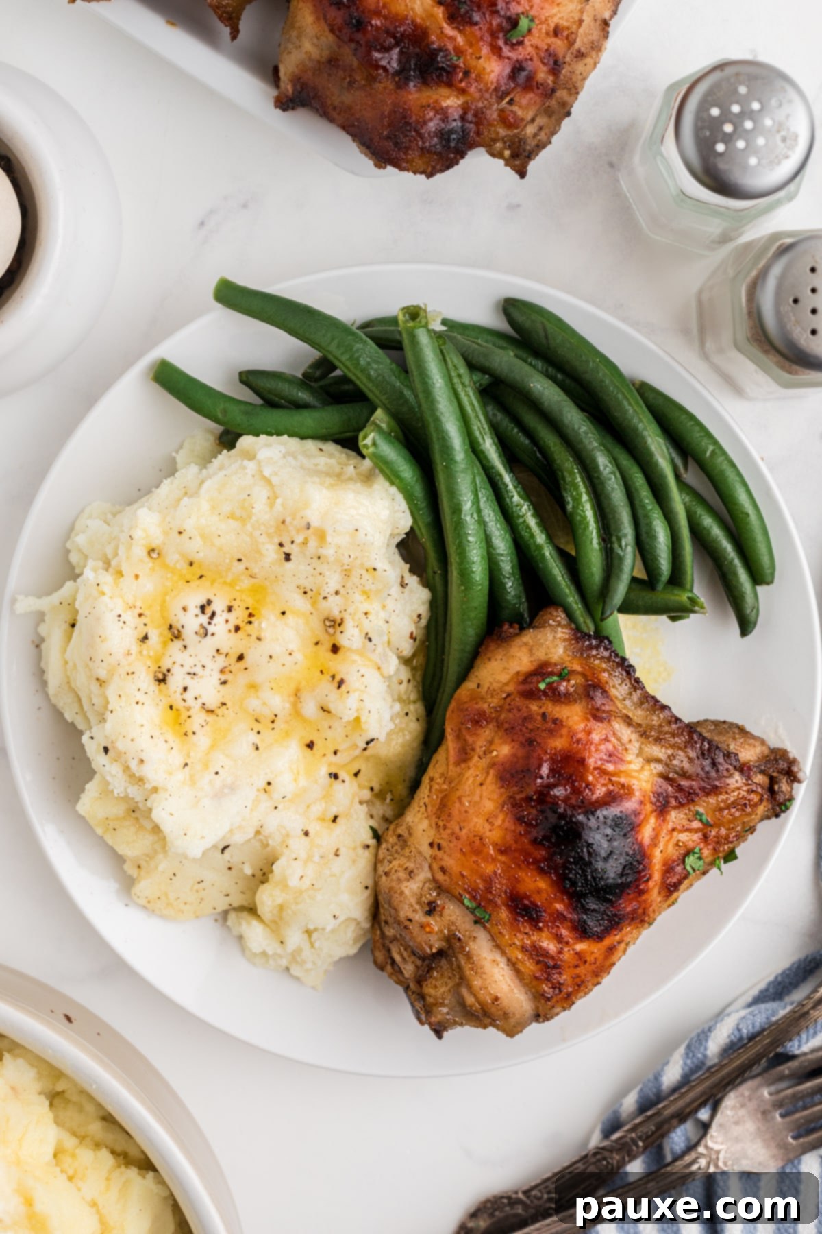 Golden Baked Chicken Thighs 9 A plate featuring creamy mashed potatoes, vibrant green beans, and a perfectly cooked crispy chicken thigh, ready for a comforting meal.