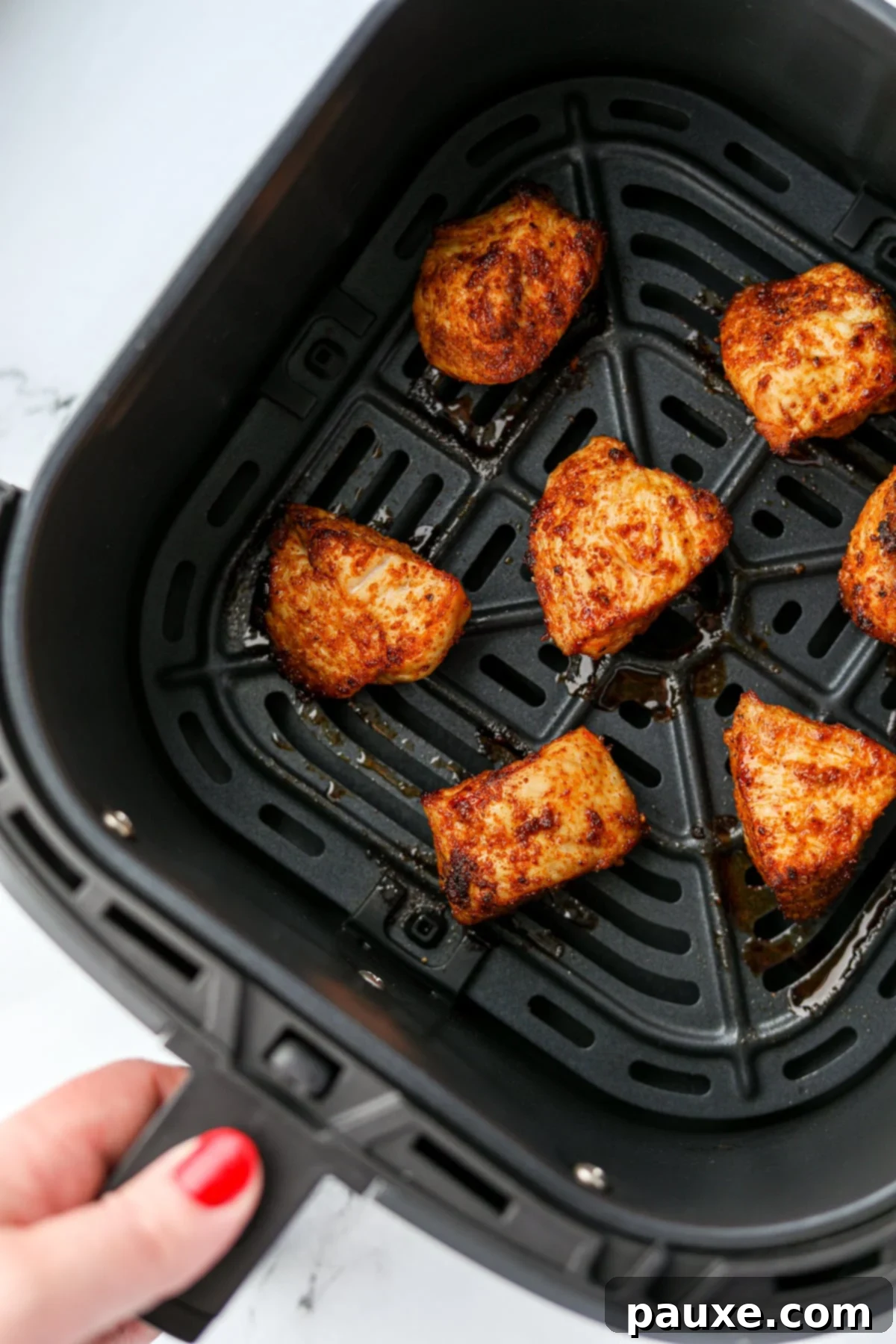 Golden Air Fryer Chicken Poppers 2 An air fryer basket with several pieces of cooked chicken inside.