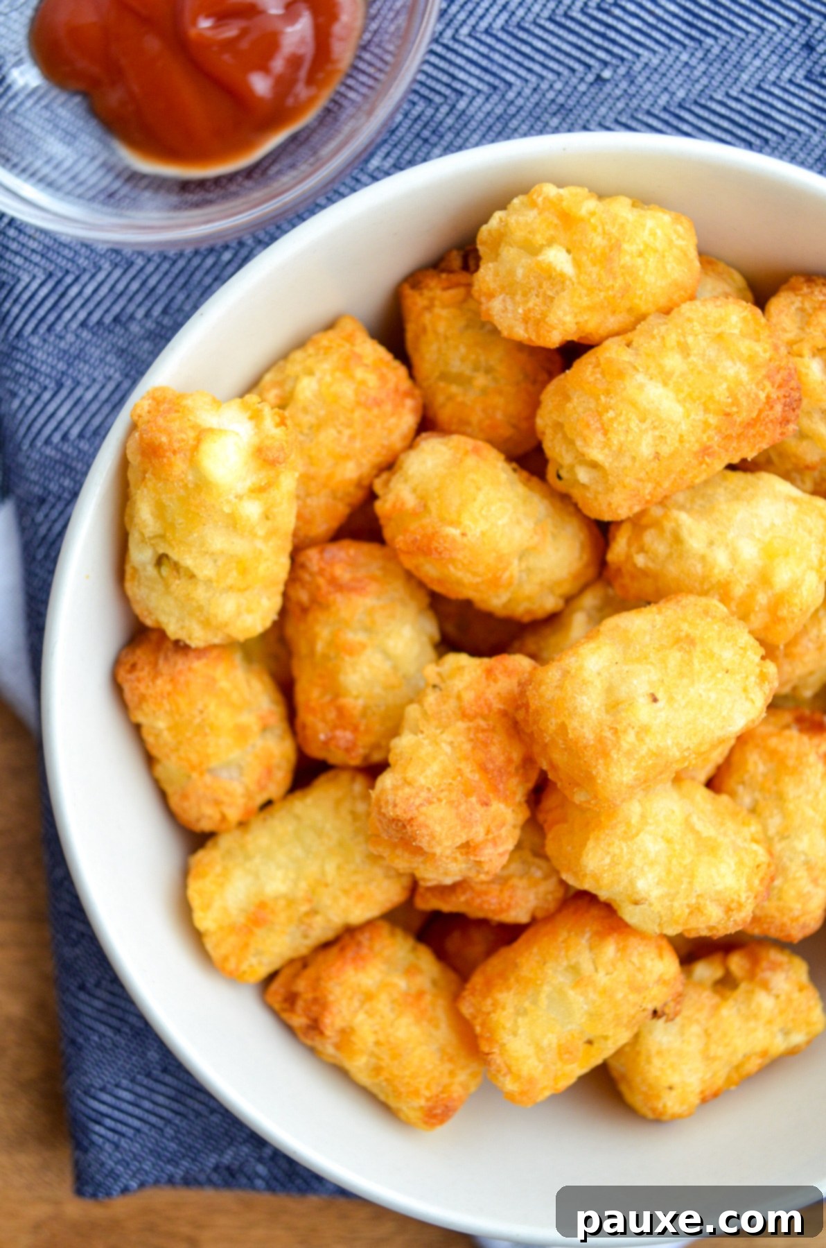 Crispy Air-Fried Tater Tots 2 A bowl of perfectly golden and crispy air fryer tater tots, with a side of ketchup for dipping.