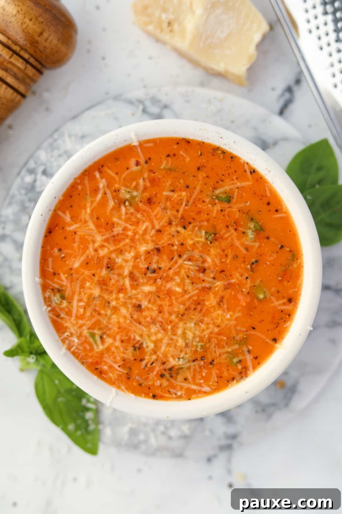Sweet & Smoky Tomato Bisque 2 A beautifully presented bowl of creamy roasted cherry tomato soup, garnished generously with freshly shredded Parmesan cheese and a sprig of basil.