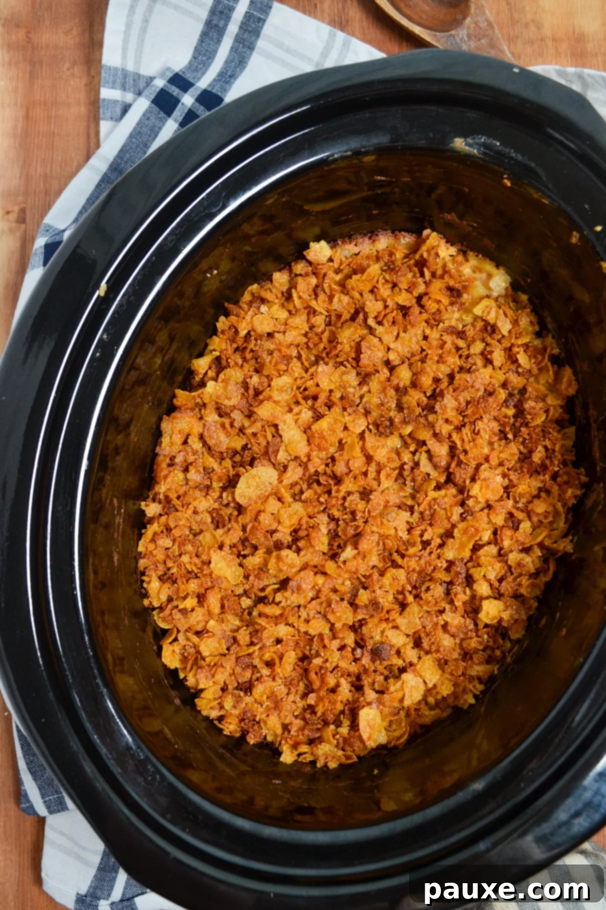 Slow Cooker Golden Cheesy Hash Brown Bake 11 A crock pot of cheesy hashbrown casserole resting on top of a napkin.