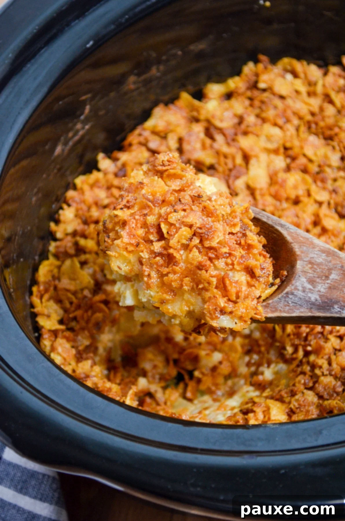 Slow Cooker Golden Cheesy Hash Brown Bake 9 A wooden spoon picks up a portion of funeral potatoes from a crock pot.