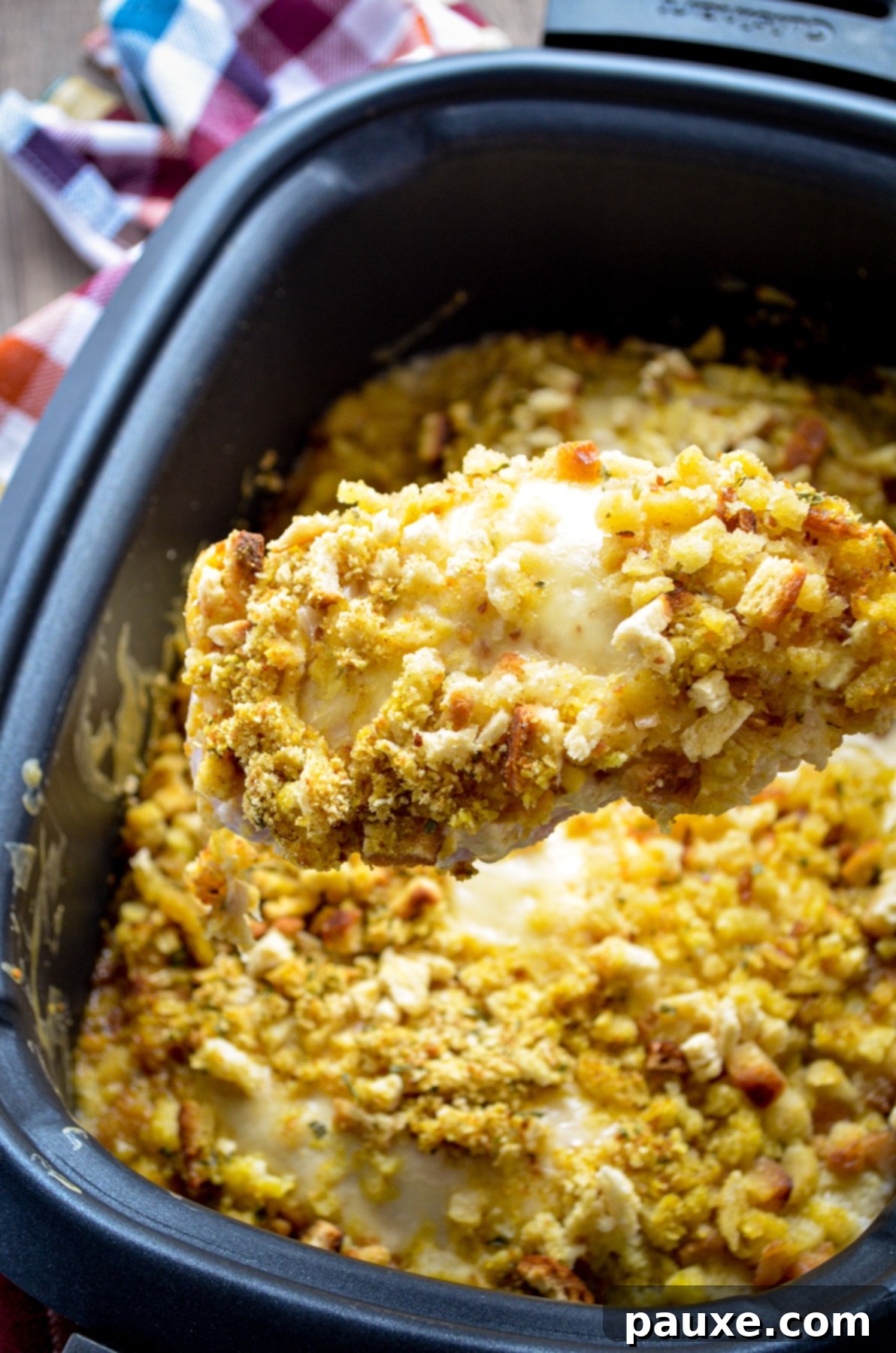 Creamy Swiss Chicken Slow Cooker Comfort 7 A wooden spoon lifting out a portion of Swiss Chicken Casserole from a Slow Cooker, showing a chicken breast covered in swiss cheese, sauce, and stuffing.