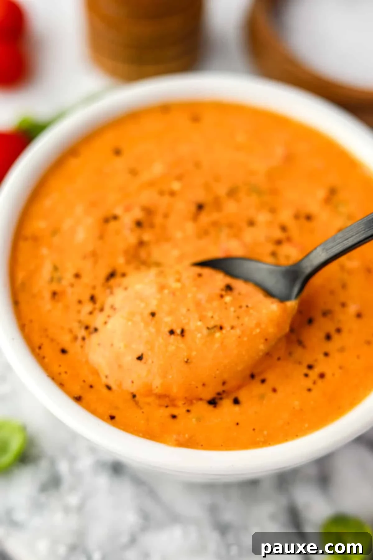 Roasted Feta Tomato Soup 6 A close-up shot of a spoon dipping into a bowl of creamy tomato soup, highlighting its smooth texture.