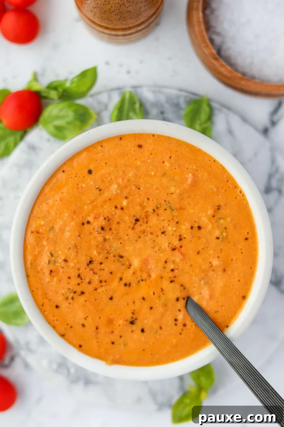 Roasted Feta Tomato Soup 7 An inviting overhead view of a bowl of creamy tomato soup, beautifully presented with fresh basil and scattered cherry tomatoes on a counter.