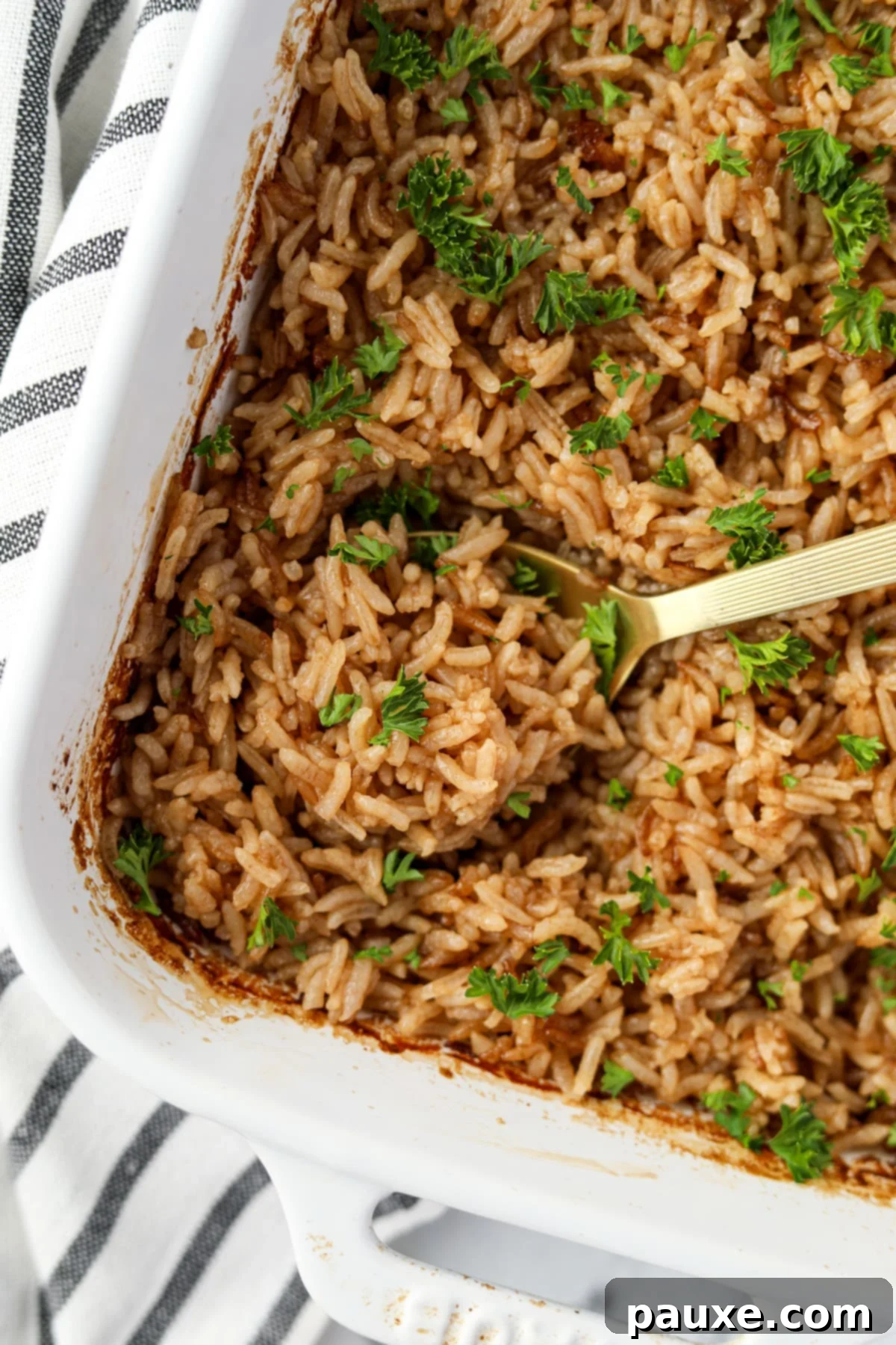 Rich Beef Consommé Rice 2 A pristine white baking dish filled with golden-brown baked rice, elegantly garnished with freshly chopped parsley, ready to be served.