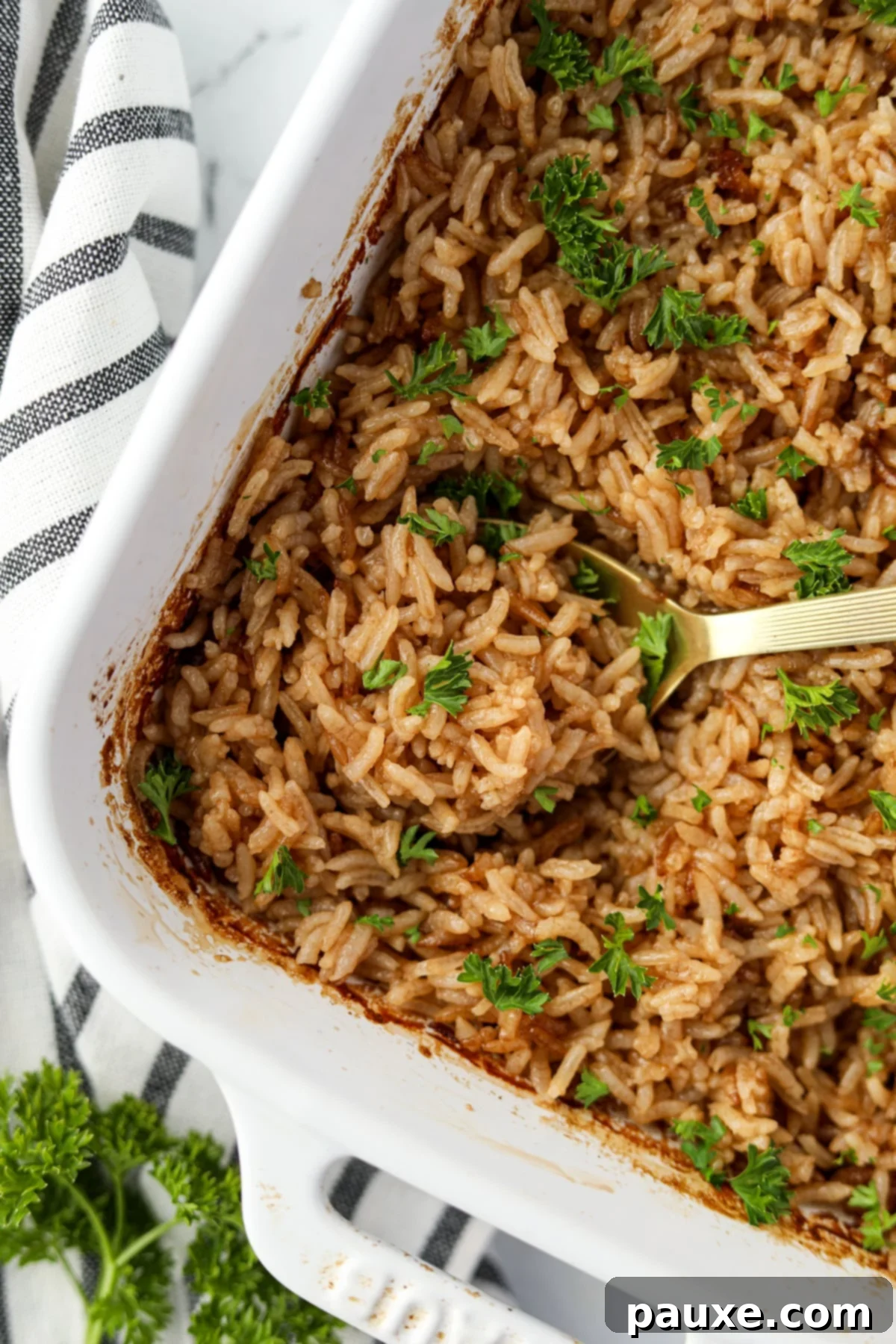 Rich Beef Consommé Rice 6 A large serving spoon elegantly rests in a baking dish, poised to scoop another portion of the golden, perfectly cooked rice.