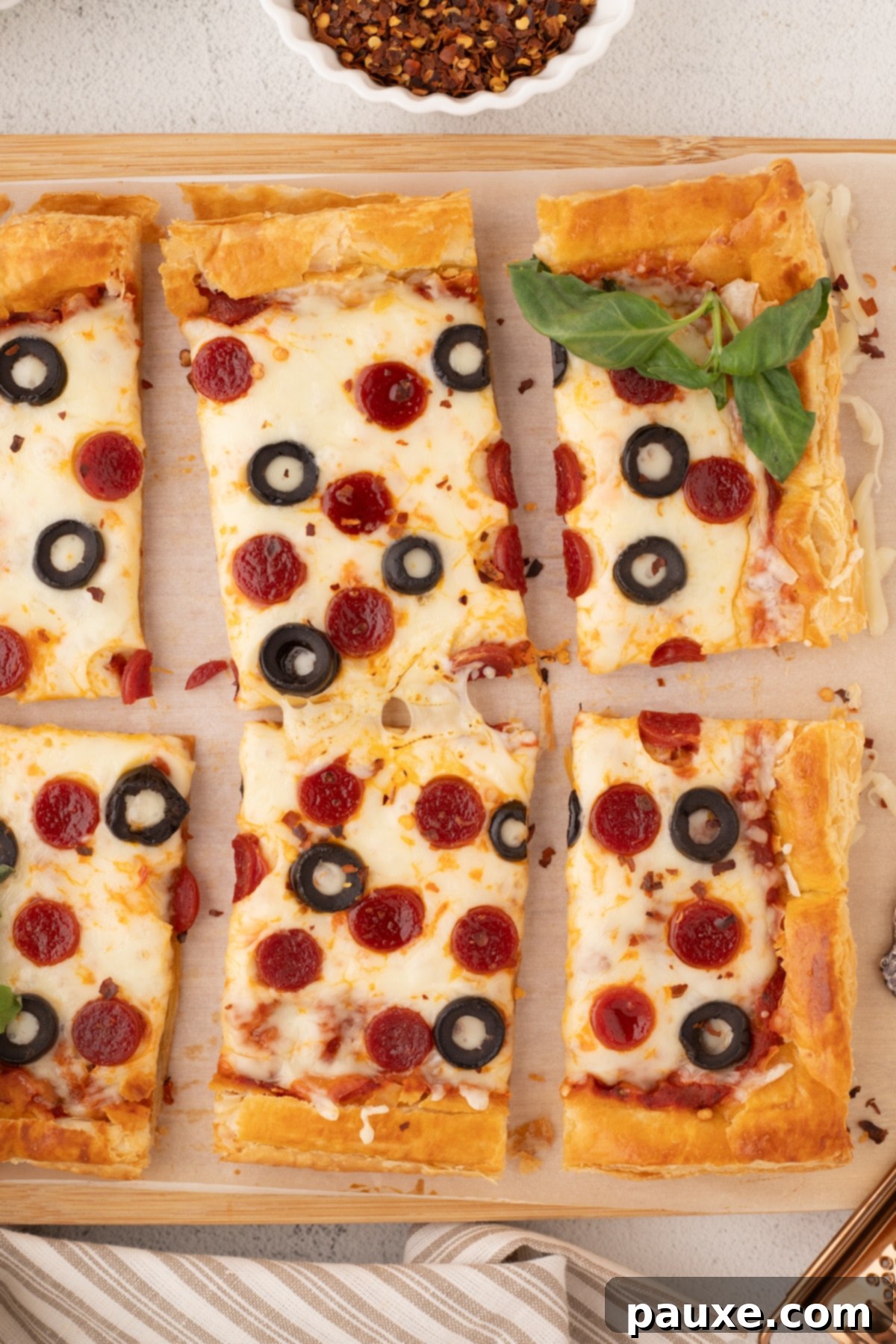 Crispy Puff Pizza 5 Slices of puff pastry pizza on a wooden cutting board, garnished with fresh basil.