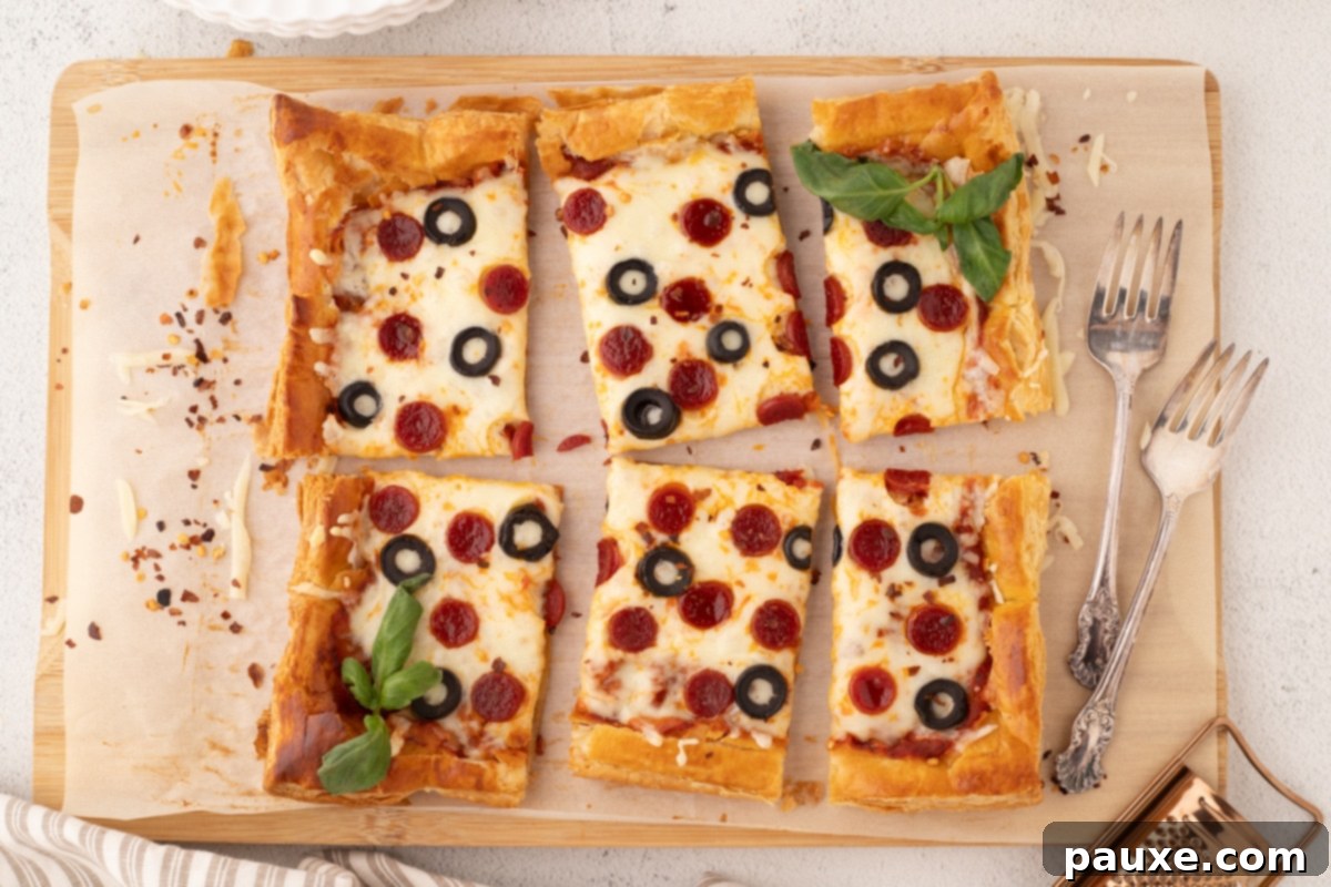 Crispy Puff Pizza 7 Slices of puff pastry pizza on a wooden cutting board topped with pepperoni, olives, and fresh basil, ready for sharing.