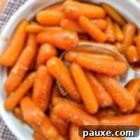 Caramelized Maple Brown Sugar Slow Cooker Carrots 11 A bowl of maple glazed carrots, with a large serving spoon taking a portion out, showcasing the rich glaze.