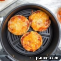 Quick Air Fryer Muffin Pizzas 10 An air fryer with english muffin pizzas in the basket, ready to cook.