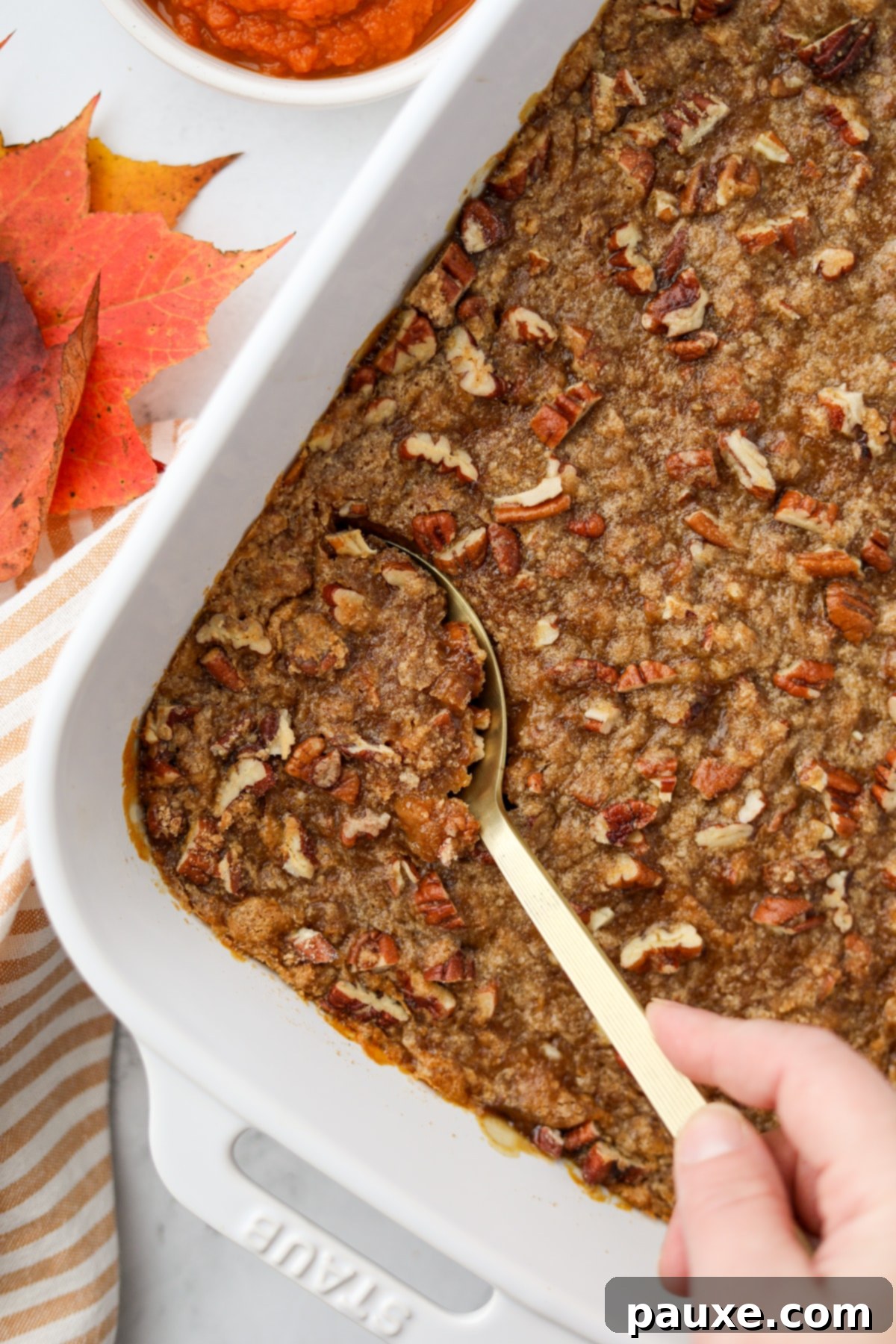 Golden Pumpkin Delight 6 A pecan streusel topped pumpkin casserole, with a golden serving spoon expertly taking a generous, creamy portion from the baking dish, highlighting its rich texture.