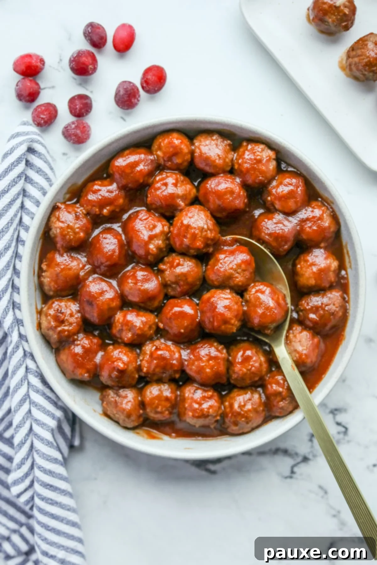 Slow Cooker Cranberry Glazed Meatballs 7 A bowl filled with glazed meatballs, with a spoon taking a portion of them.