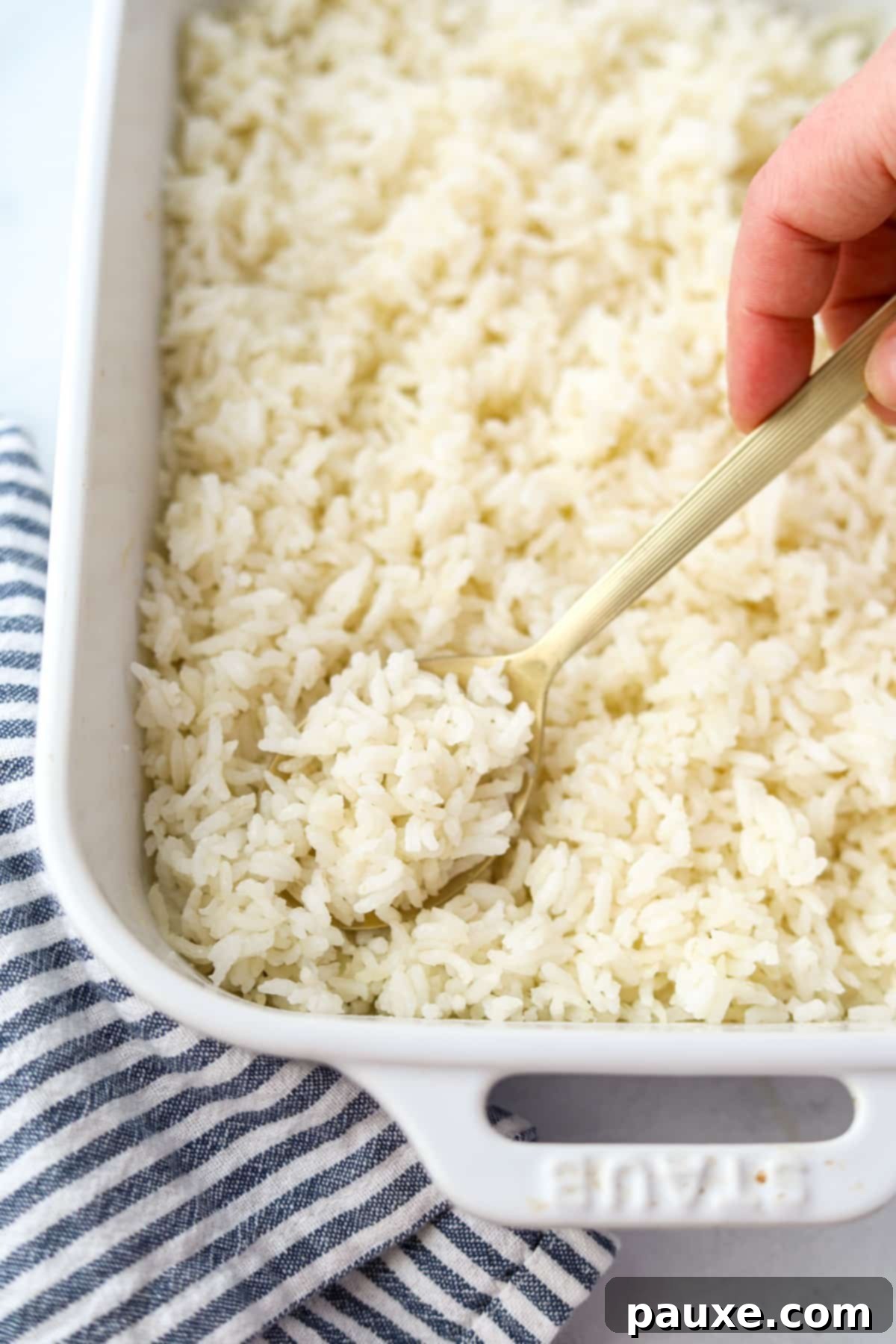 Golden Baked Rice 7 A hand holding a spoon that is scooping perfectly cooked rice from a casserole dish, showcasing its fluffy texture.