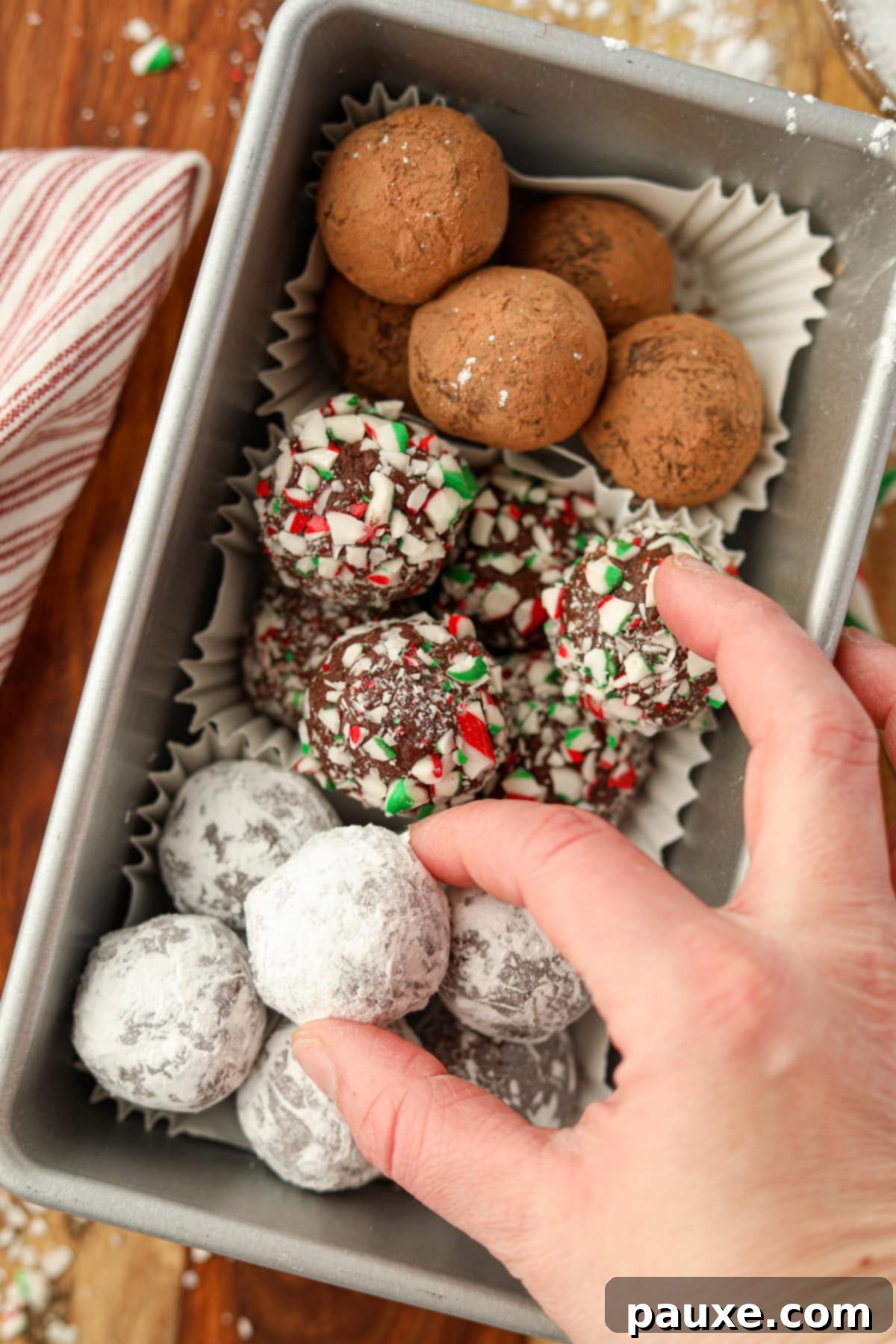 Refreshing Peppermint Truffles 11 A hand taking a powdered sugar coated chocolate ball from a container.