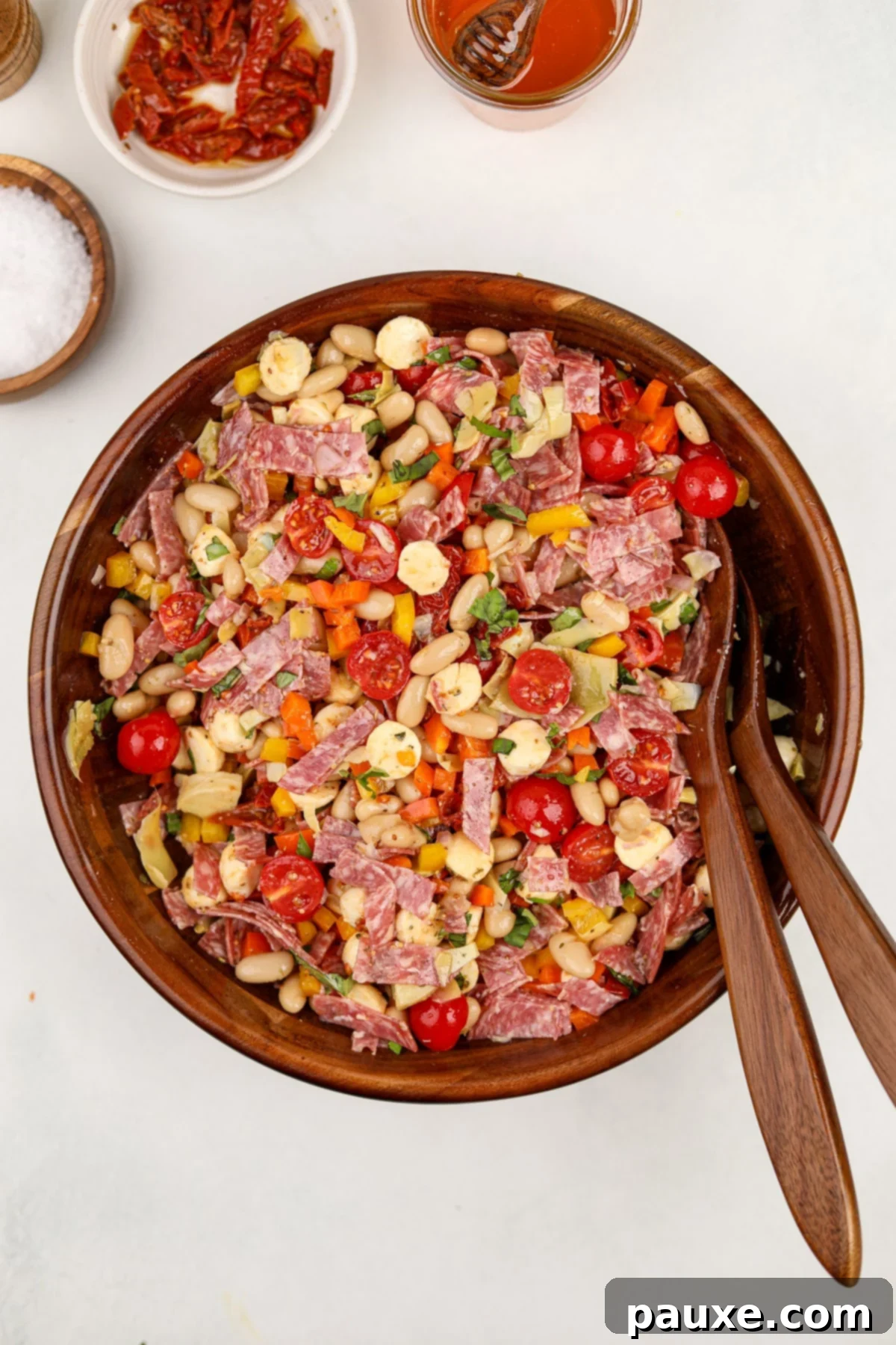 Hearty Italian Bean Medley 5 A salad bowl filled with salad featuring white beans, cherry tomatoes, salami, and mini mozzarella balls.