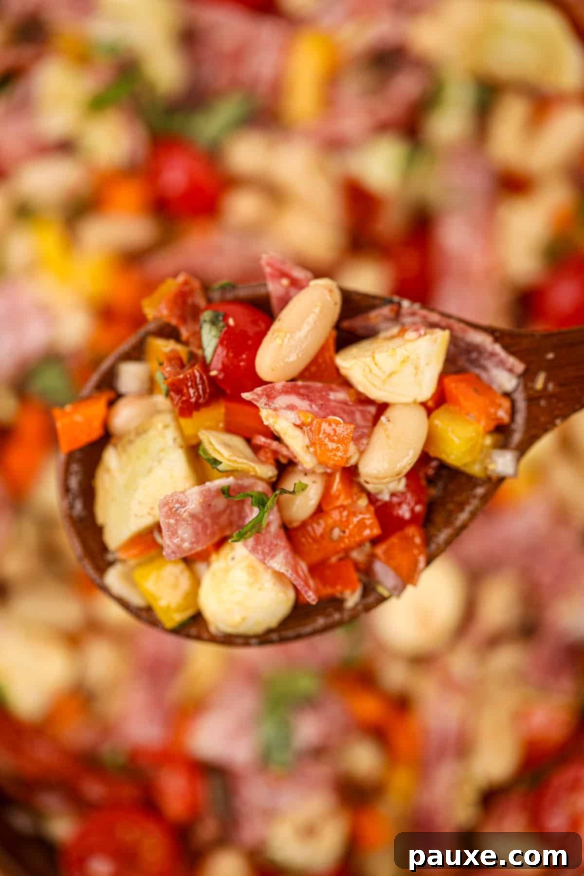 Hearty Italian Bean Medley 8 A wooden spoon holding up a small portion of white bean salad with salami and sun-dried tomatoes.