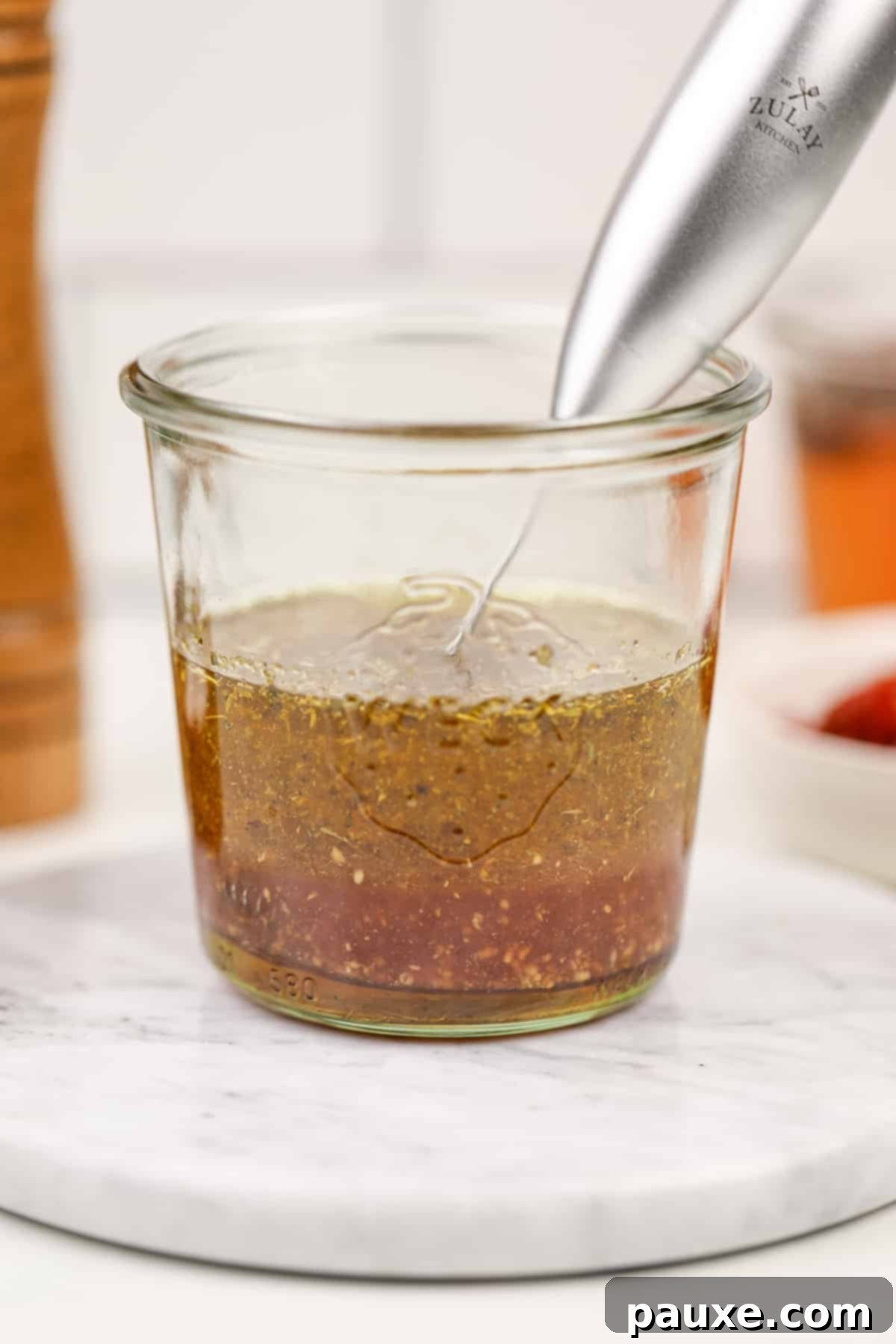 Mediterranean Sunset Vinaigrette 5 A glass jar with layers o of oil and vinegar, with a small frother want sticking out of the side.