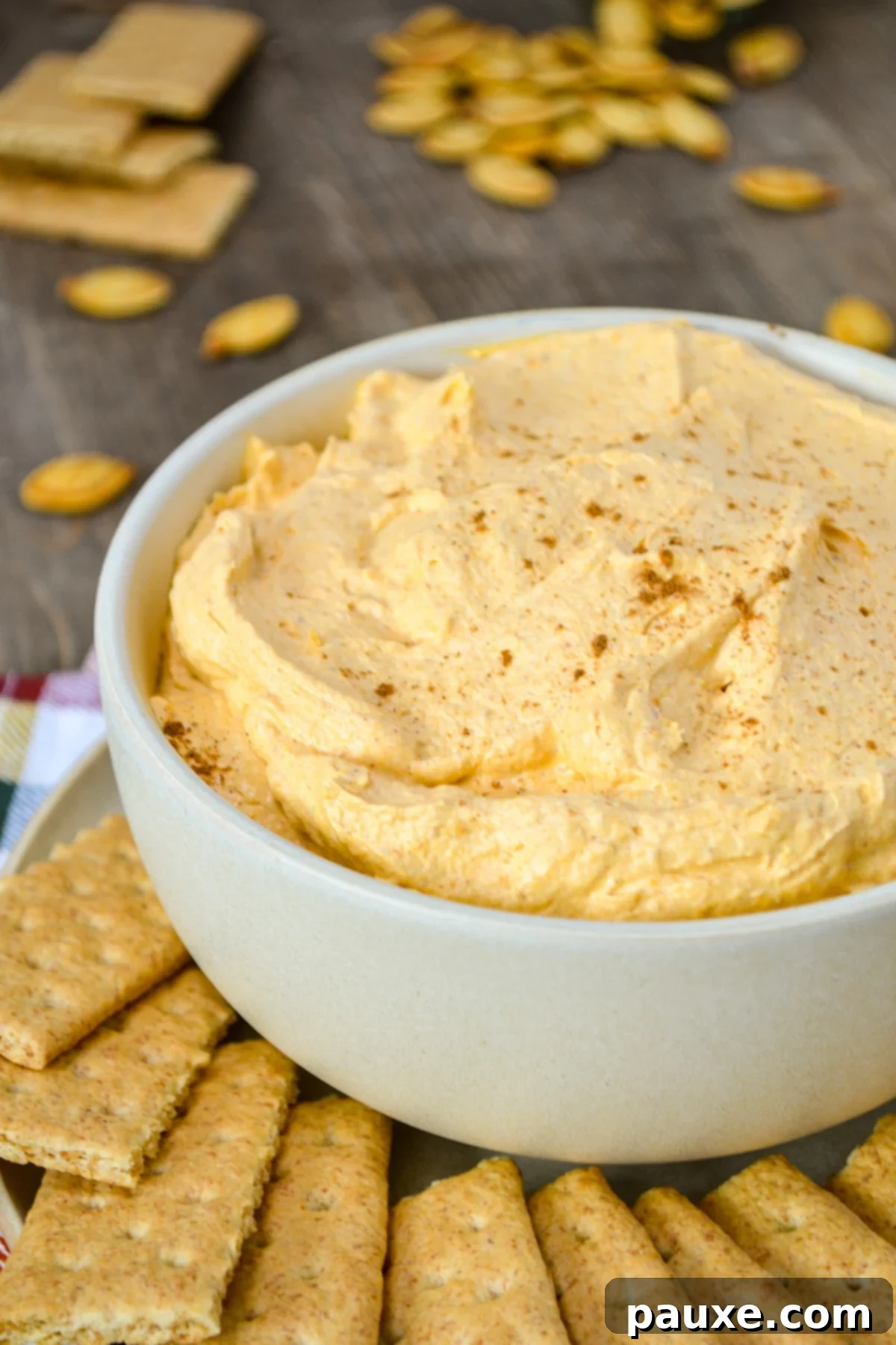 A bowl of pumpkin fluff dip, surrounded by multiple graham crackers and pumpkin seeds