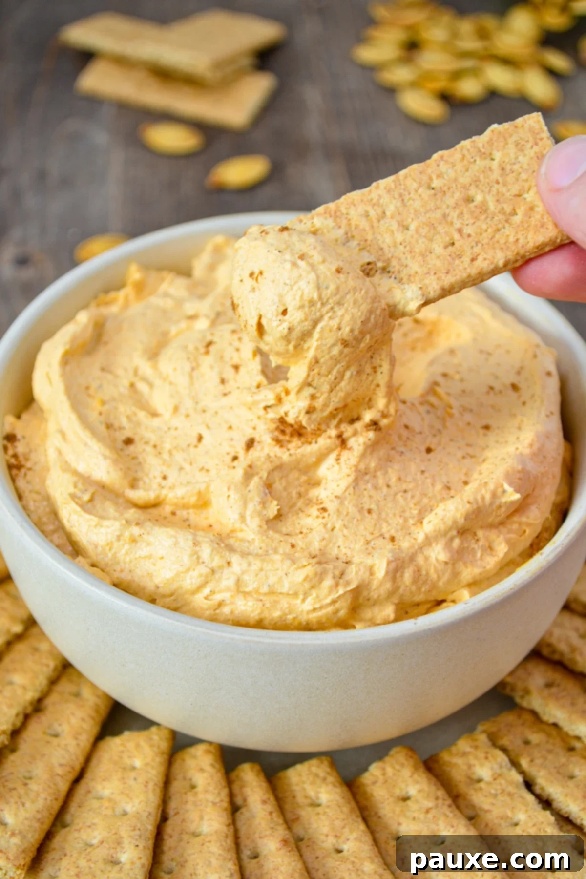 A bowl of pumpkin fluff, with a graham cracker being dipped into it.