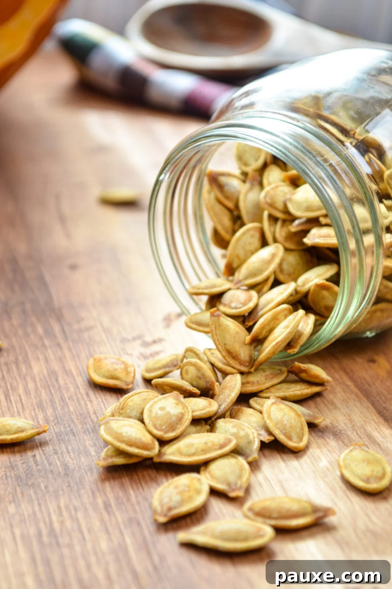 Crispy Air Fryer Pumpkin Seeds 2 A charming glass jar overflowing with roasted pumpkin seeds, spilling onto a rustic wooden table. A perfect autumn snack scene.