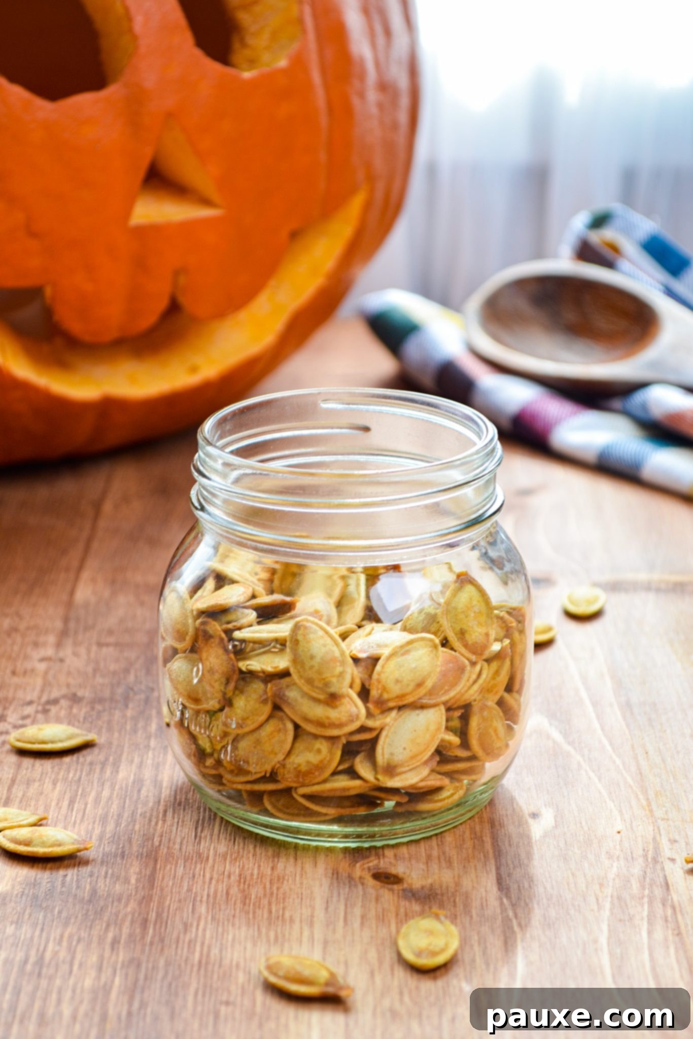 Crispy Air Fryer Pumpkin Seeds 9 A beautifully composed shot of a jar brimming with perfectly roasted pumpkin seeds, with a soft-focus, carved Halloween pumpkin in the background, creating an autumnal vibe.