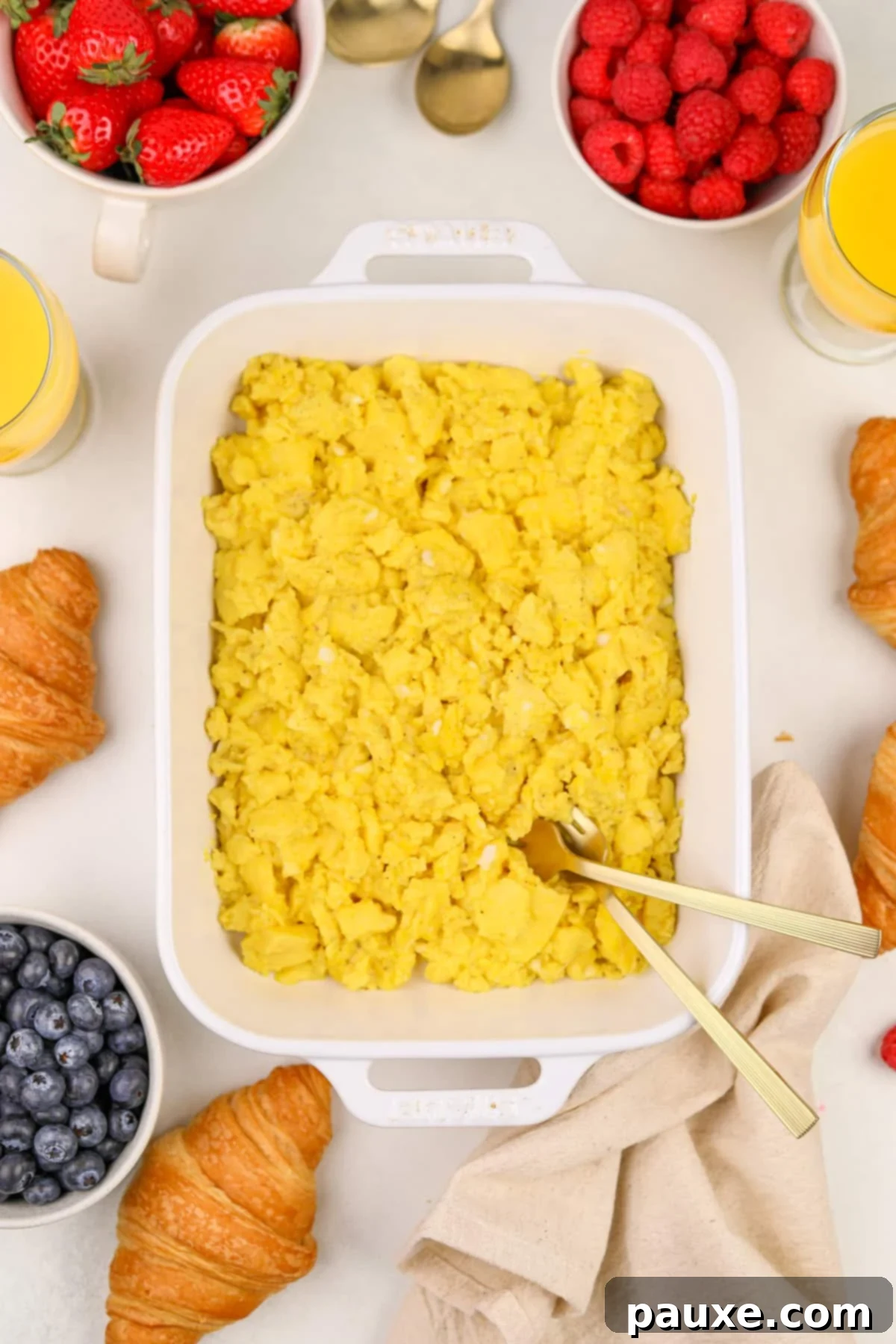 Fluffy Oven Scramble 5 A white baking dish filled with cooked eggs, surrounded by fresh berries.
