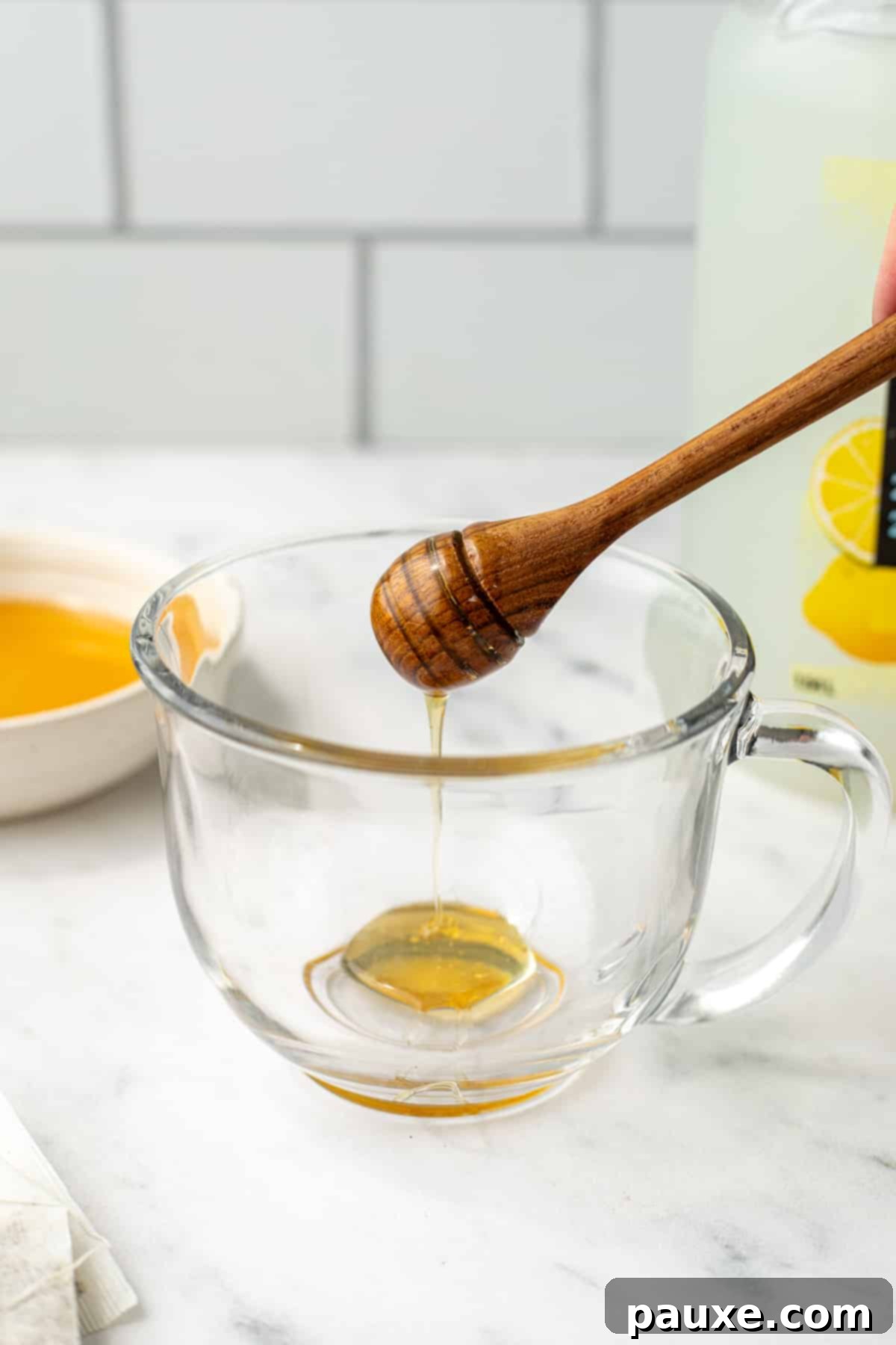Drizzling honey into a glass mug.