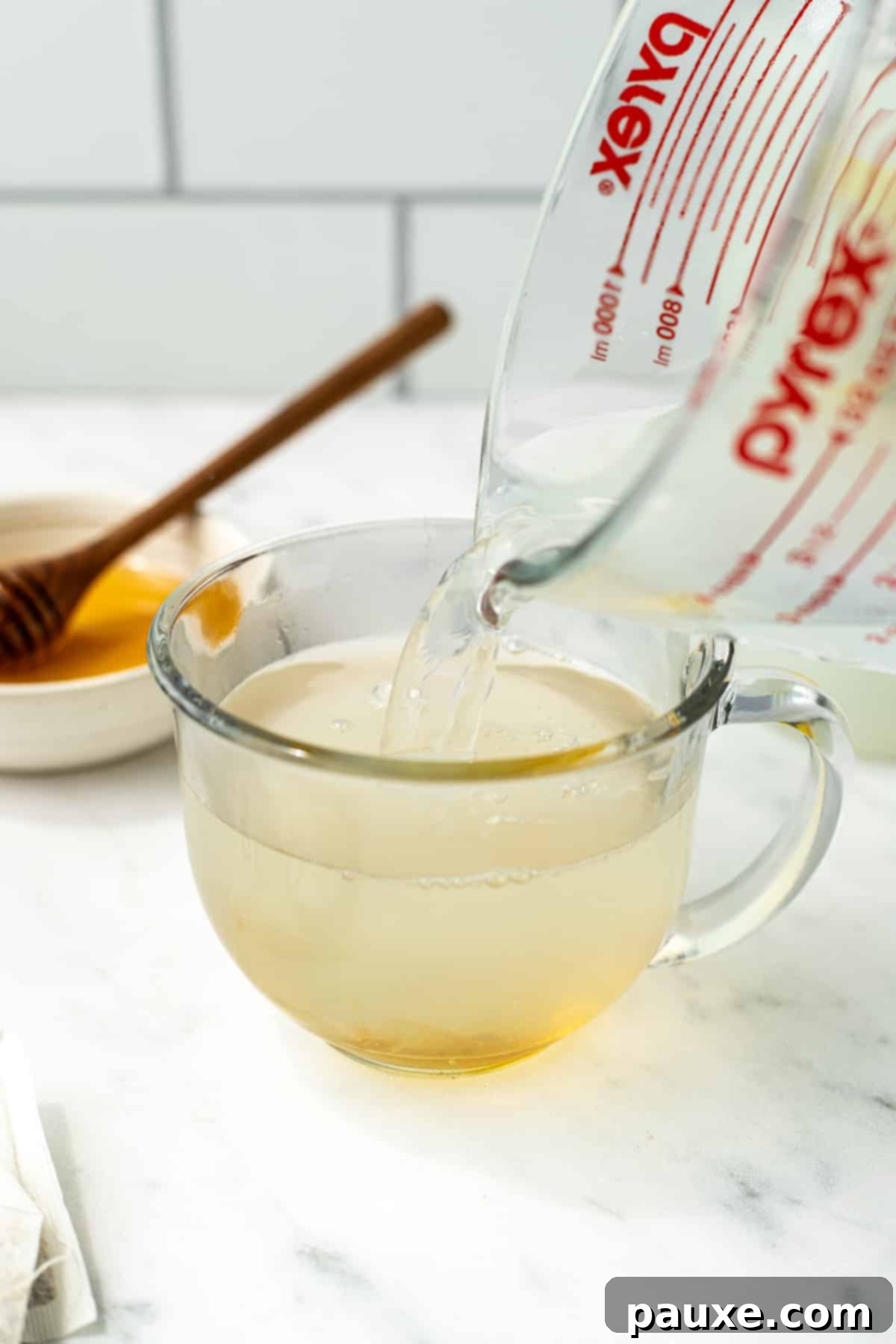 Pouring hot liquid into a glass mug with honey at the bottom.