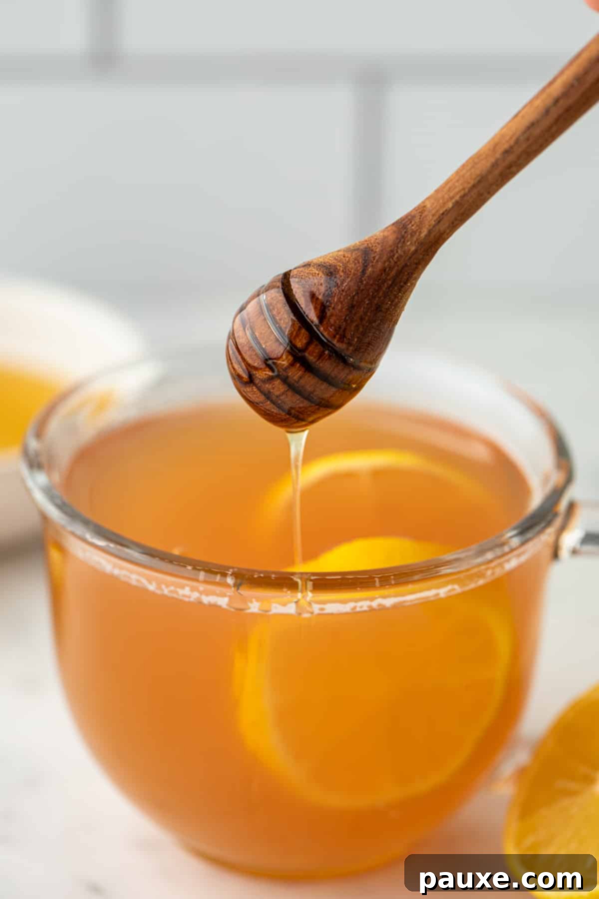 Drizzling honey in a glass of steeped tea garnished with lemon slices.