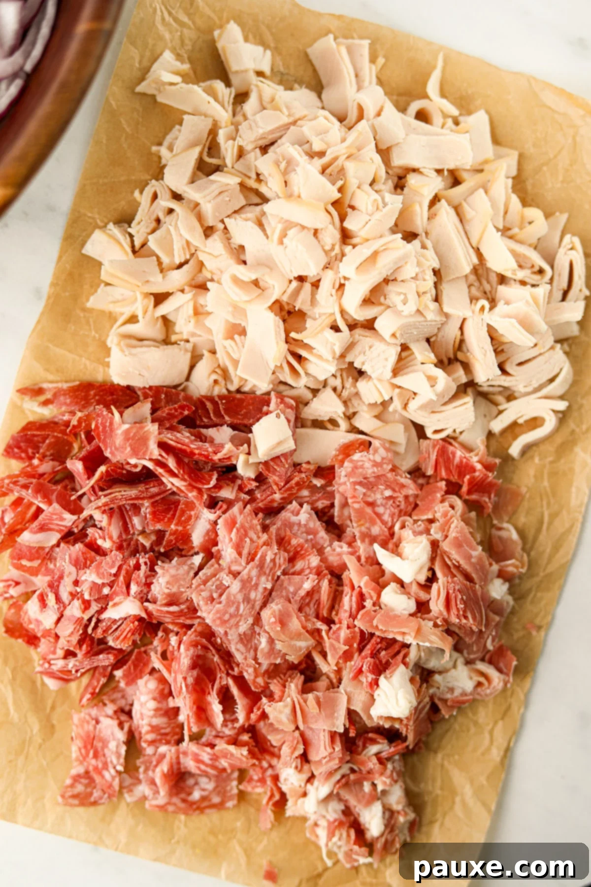 Hero Salad Bowl 4 A neatly piled mound of finely chopped deli meat on a sheet of parchment paper, ready for the grinder salad.