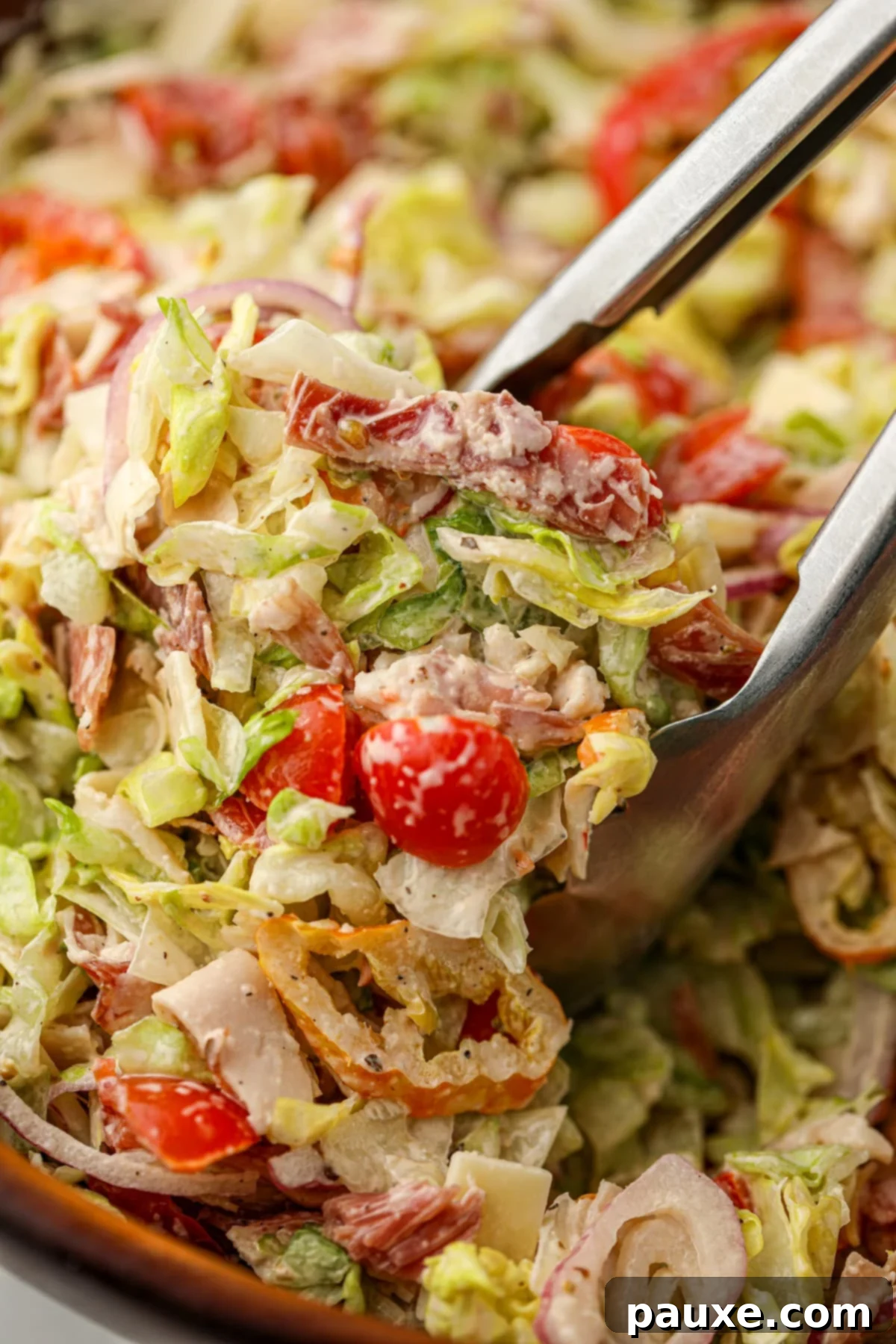 Hero Salad Bowl 6 A large pair of tongs scooping a generous portion of freshly made, creamy Grinder Salad from a wooden bowl.
