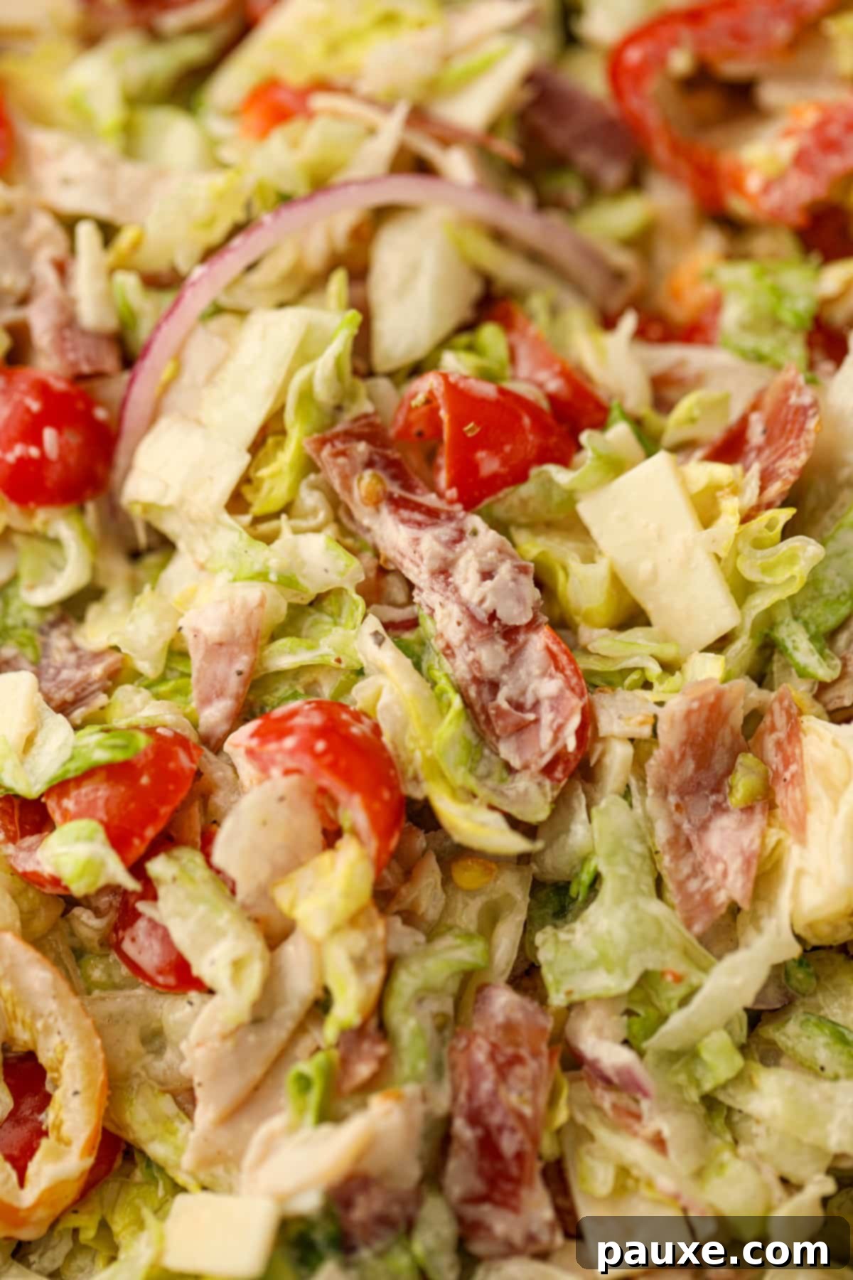 Hero Salad Bowl 8 A close-up shot of the Italian Grinder Salad, highlighting the vibrant mixture of finely chopped deli meat, juicy cherry tomatoes, crisp red onion, and tangy banana pepper coated in creamy dressing.